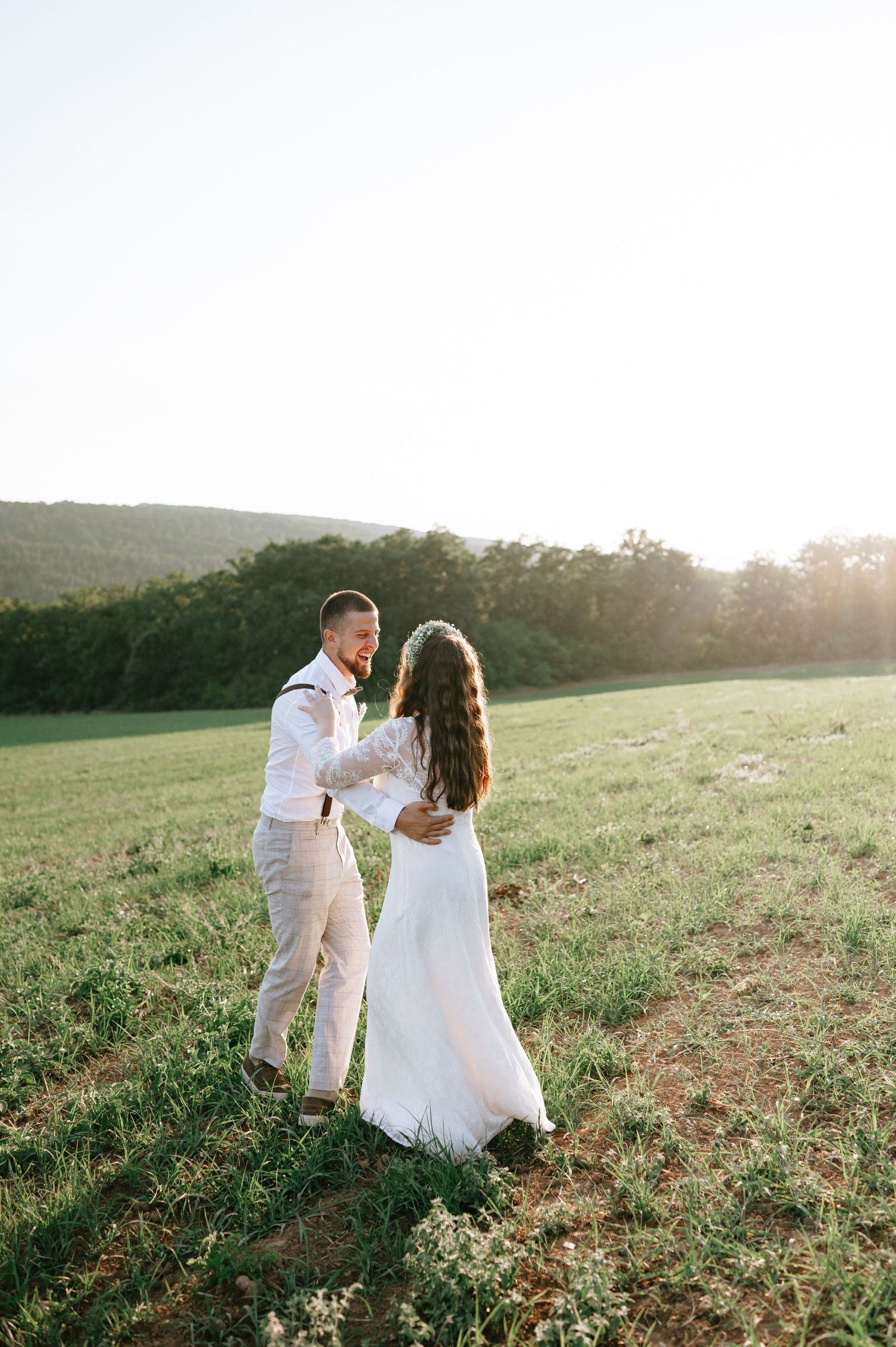A romantic couple in white attire shares an intimate moment in a sunlit meadow during golden hour.