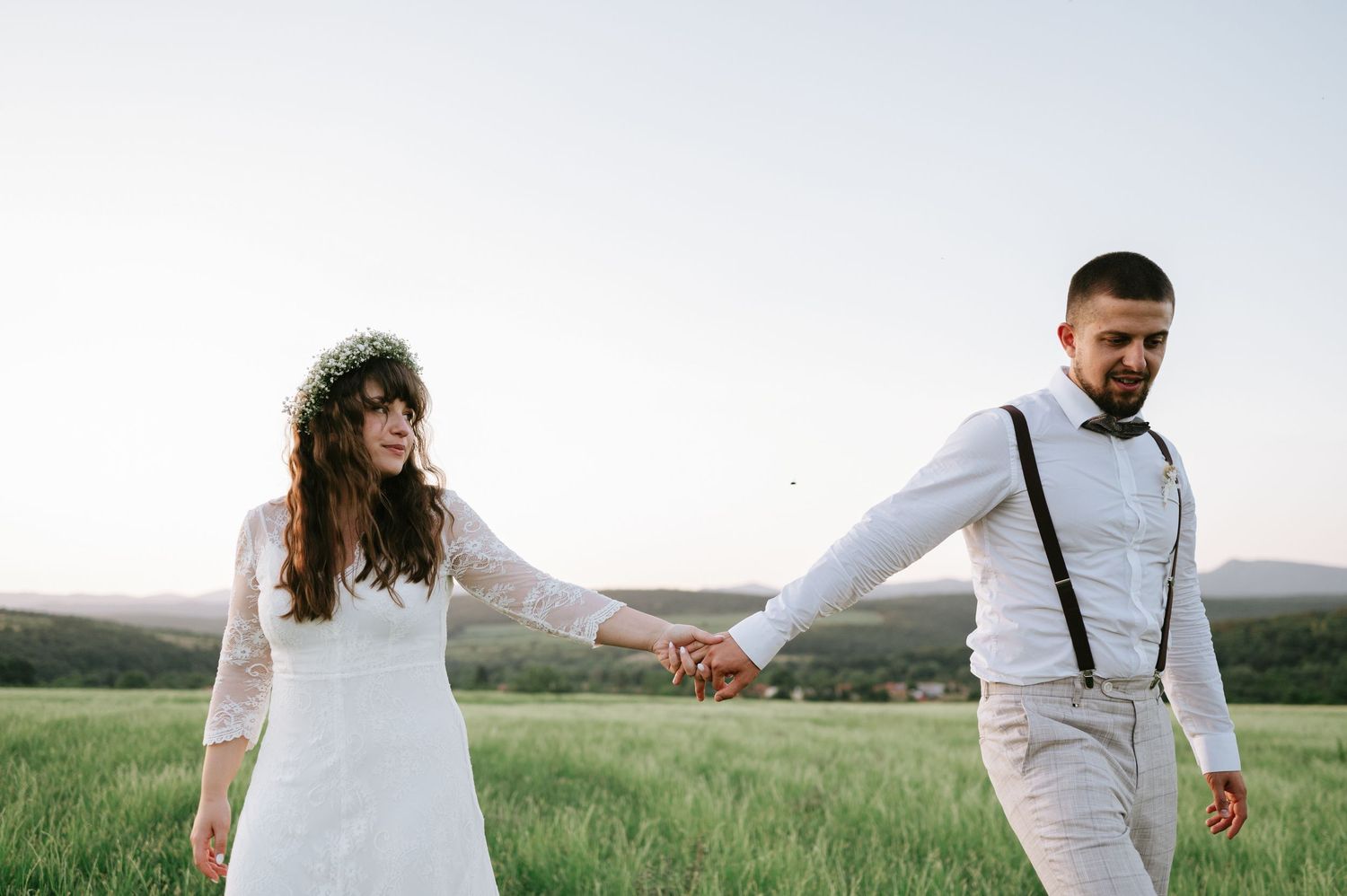 Wedding couple walking through a lush green meadow at sunset.
