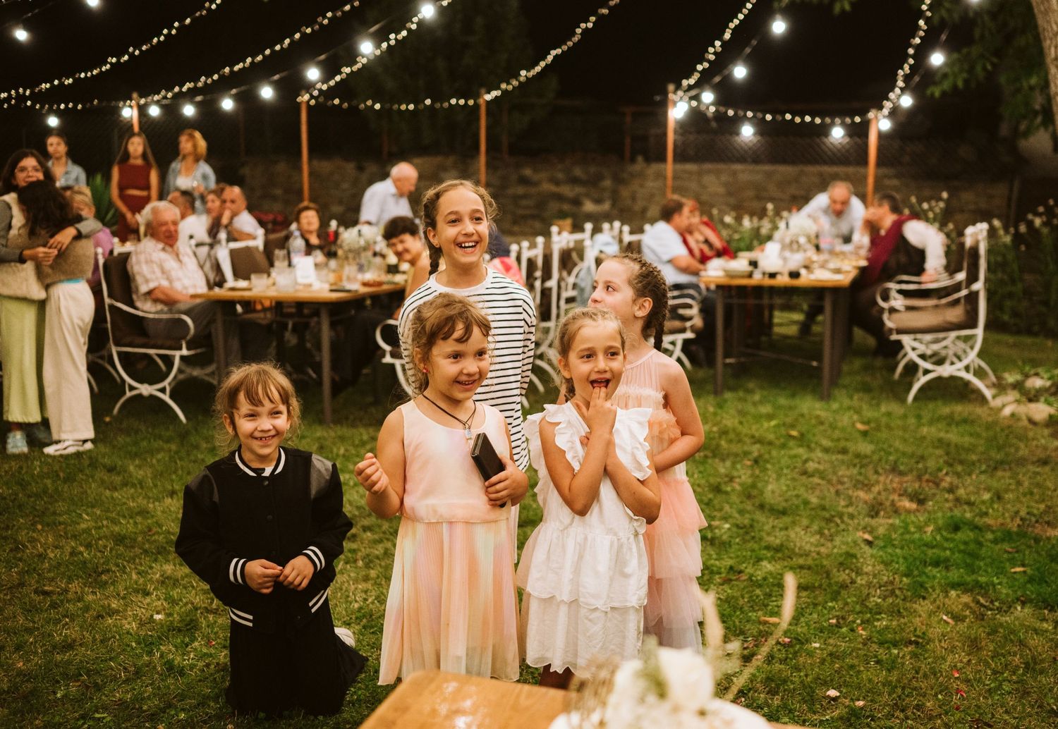 Outdoor wedding reception with string lights and guests celebrating.