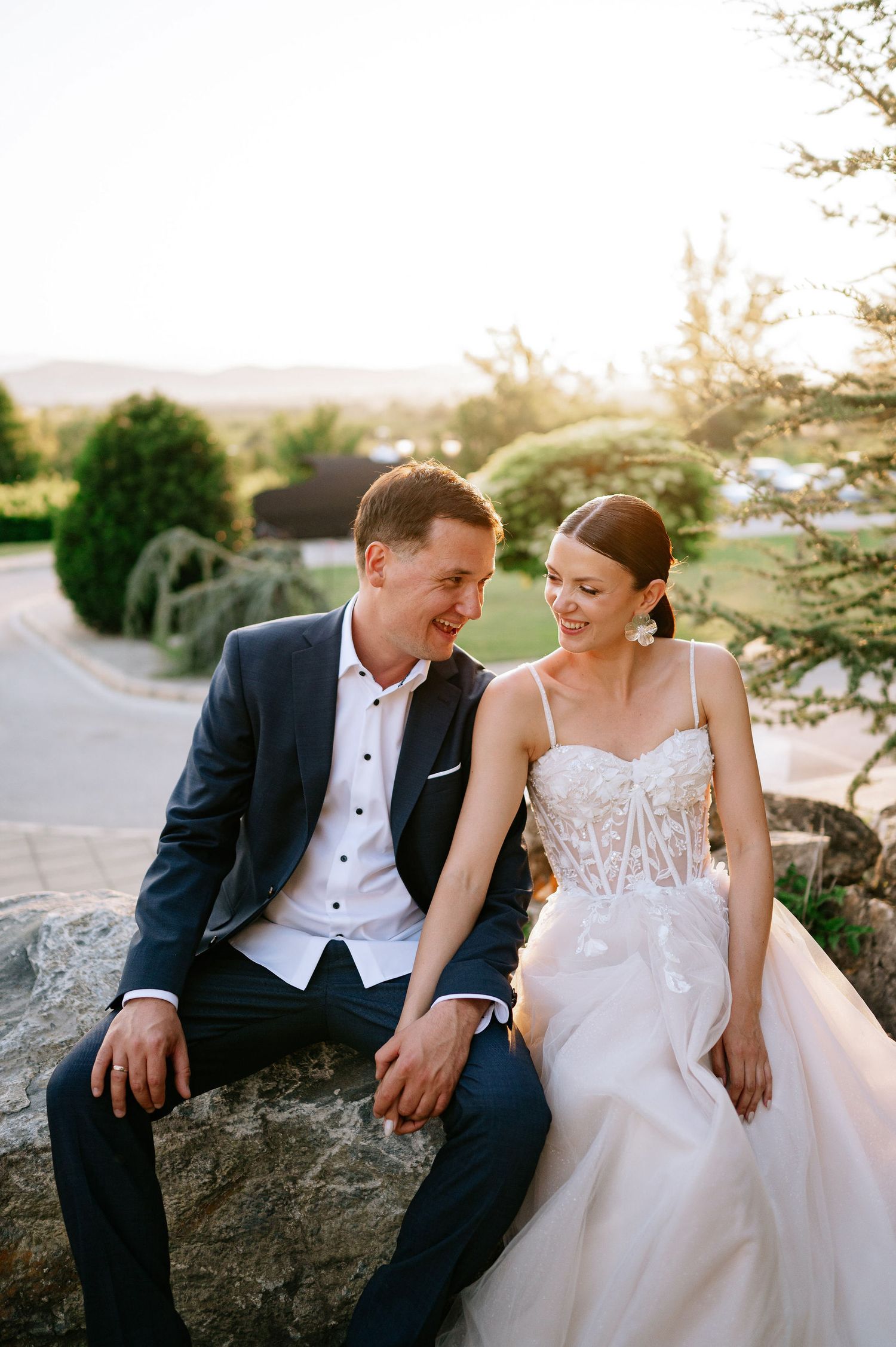 Newlyweds share an intimate moment while sitting on rocks at sunset in their wedding attire.