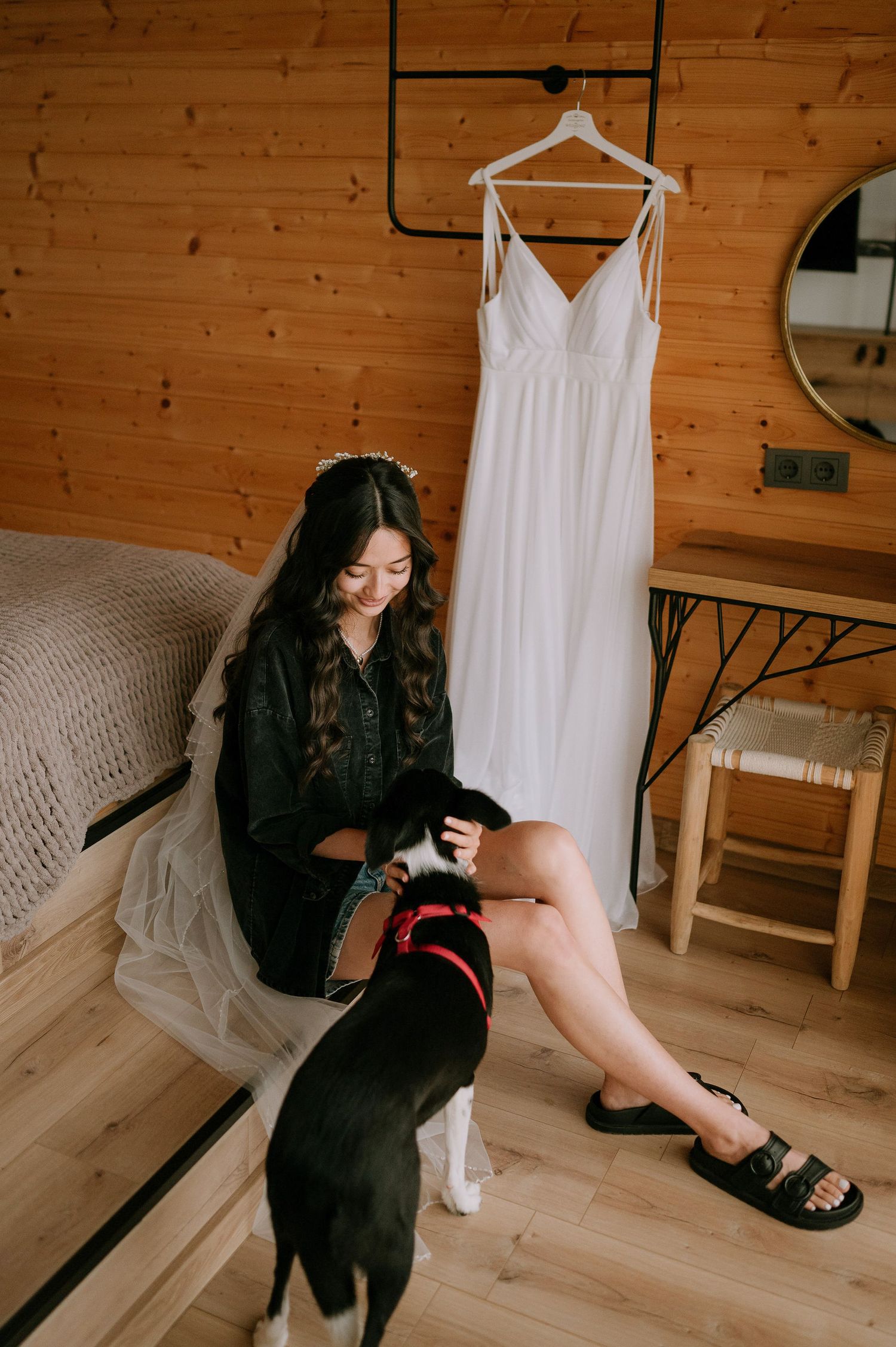 Casual indoor photoshoot featuring a black outfit against warm wooden walls and a hanging white dress.