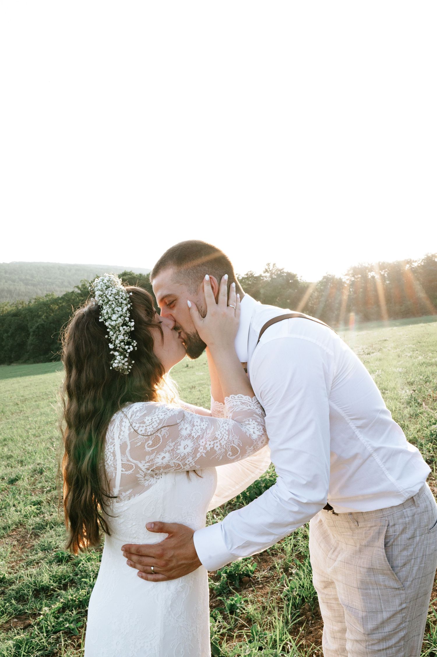 A romantic moment between newlyweds dancing in a field at sunset.