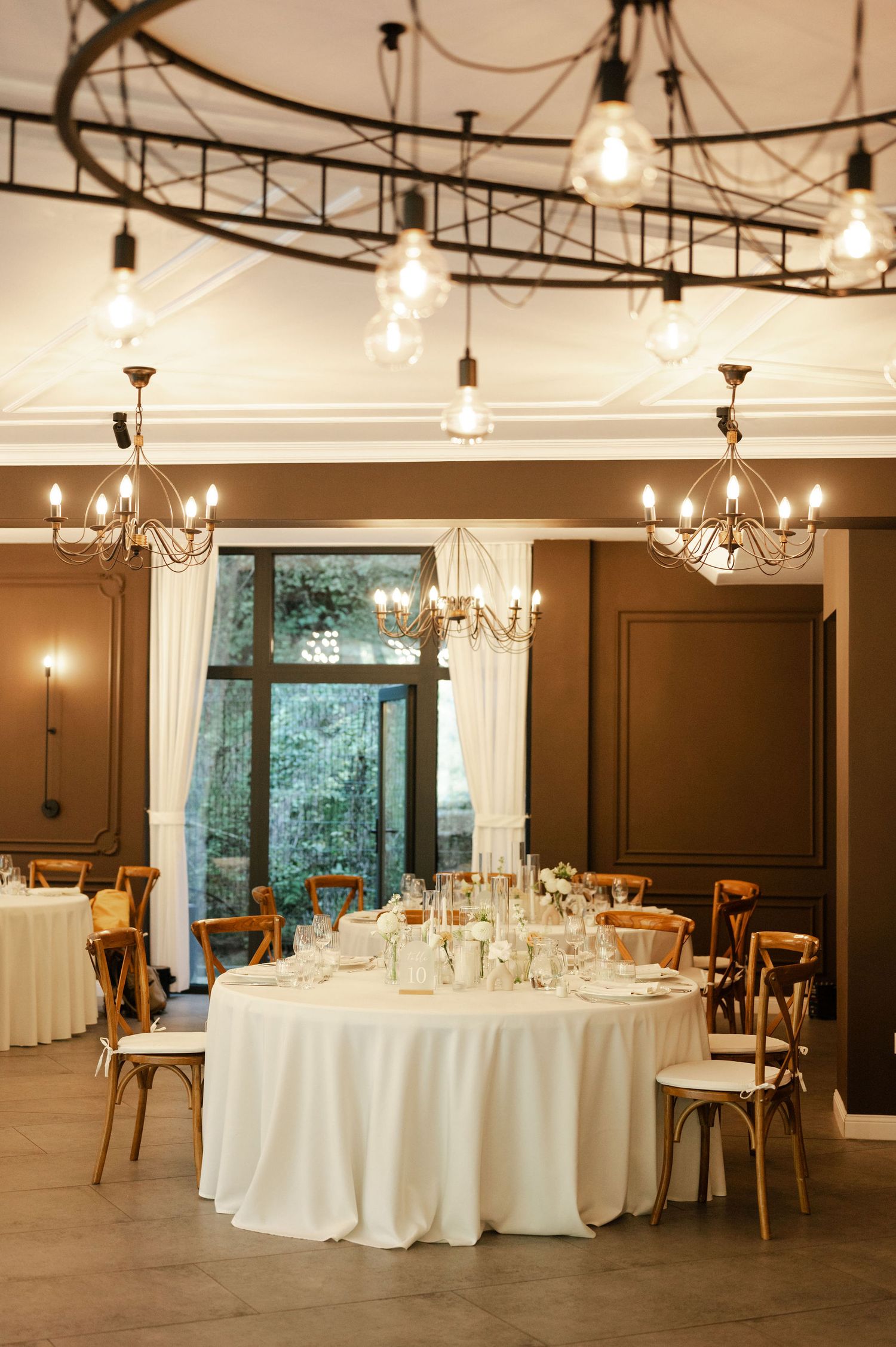 Modern reception space with round tables, chandeliers and dark accent walls creating an intimate atmosphere.
