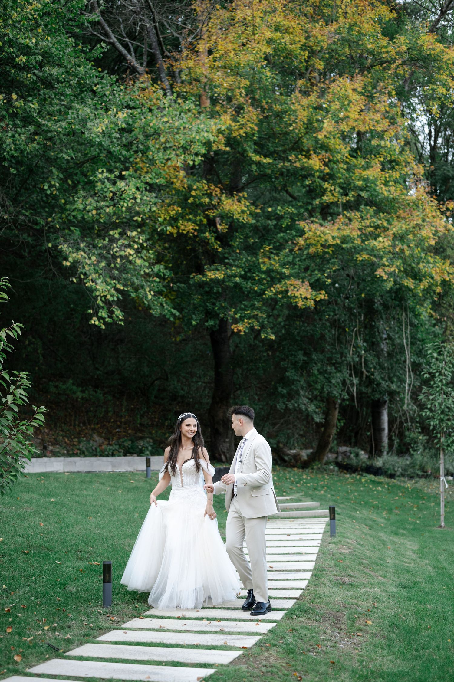 A couple descends white stone steps on a grassy hillside during their wedding photo session.