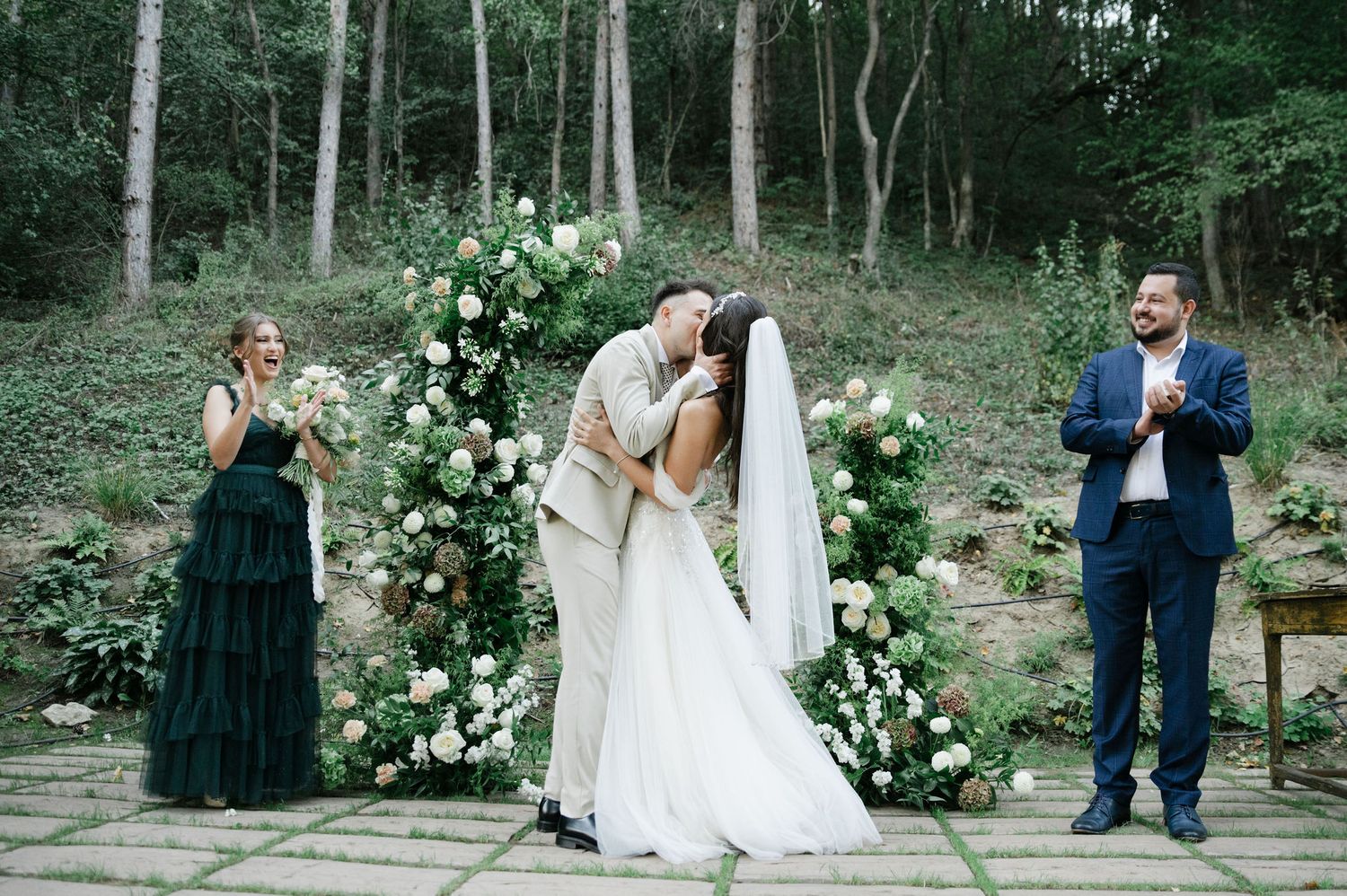 Intimate forest wedding ceremony with elegant floral arch and wedding party.