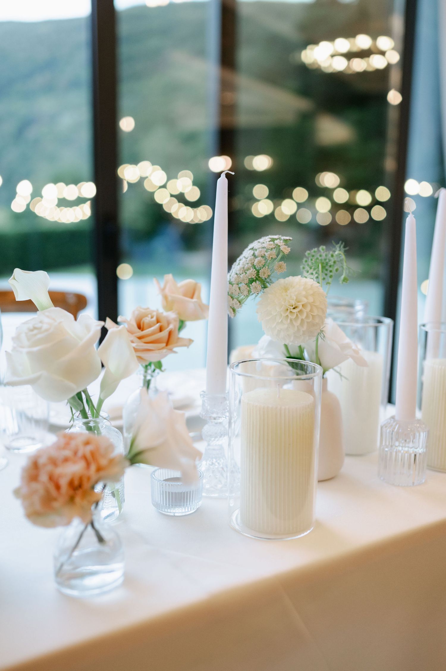 Wedding table decorations featuring white candles and soft peach flowers with mountain views beyond.
