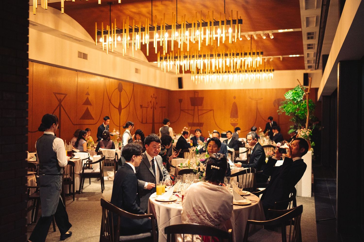 Panoramic view of an elegant dining hall filled with guests under dramatic lighting fixtures.