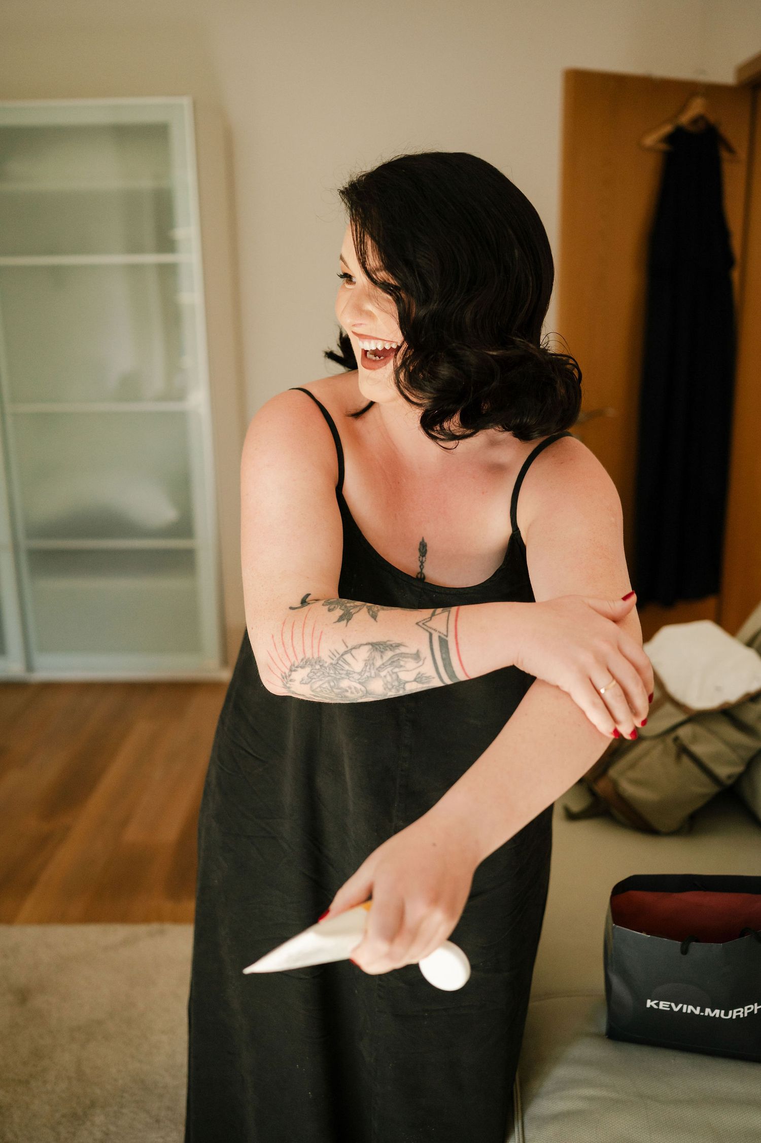 Person in black tank top holding beauty product in bright room.