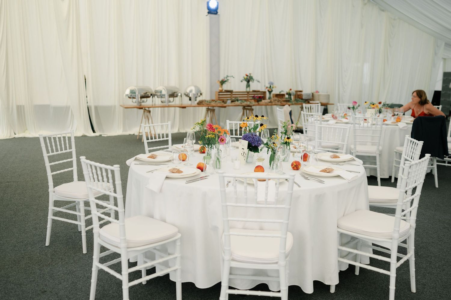 White chiavari chairs and round tables set up in a wedding tent with delicate floral arrangements.