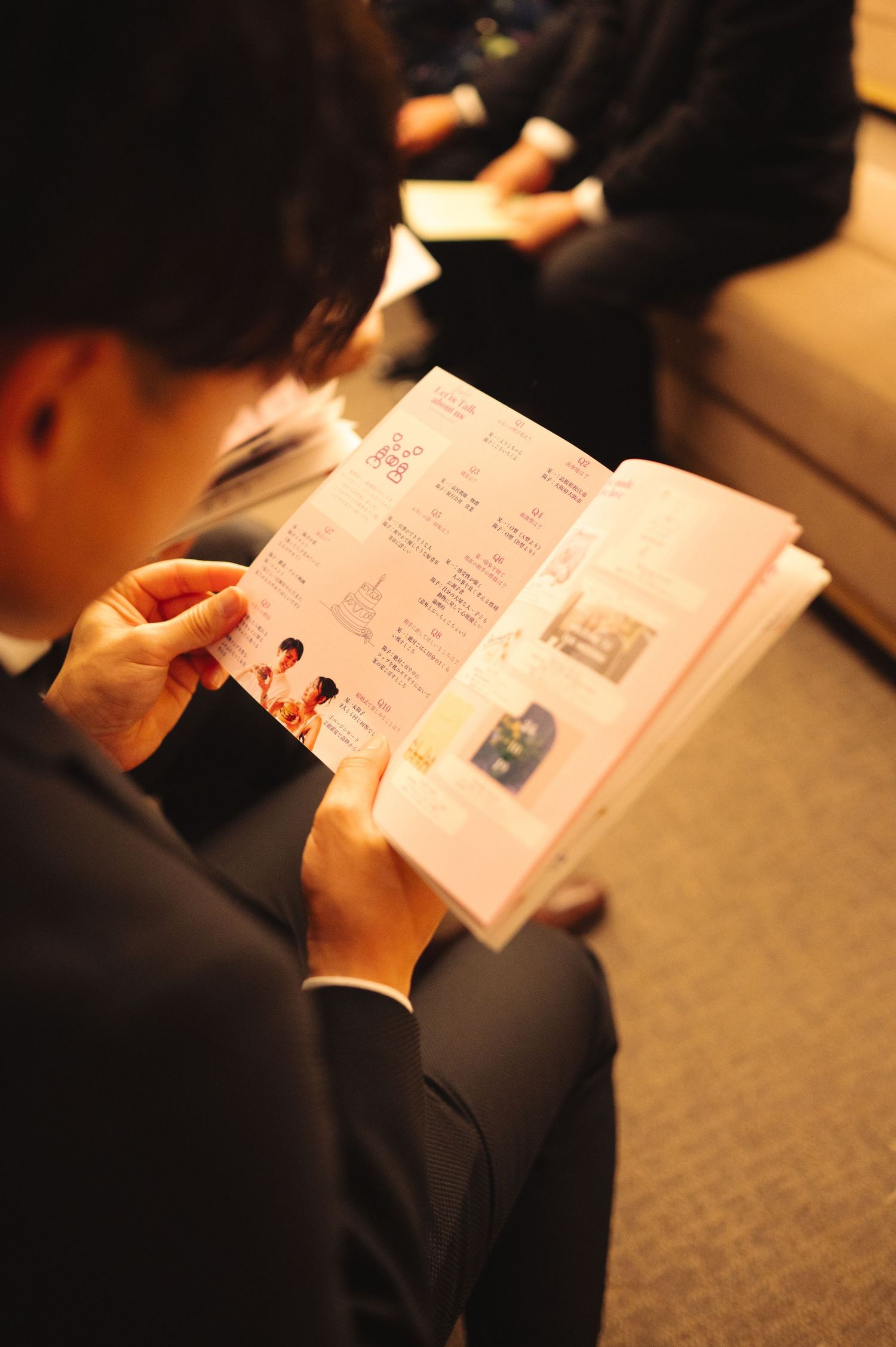 People reading through program materials in a dimly lit indoor setting.