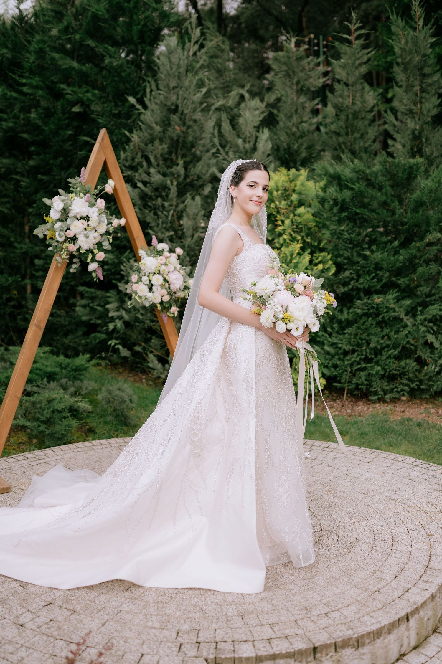 Elegant bridal portrait on circular stone patio with wooden triangle arch and floral arrangements.