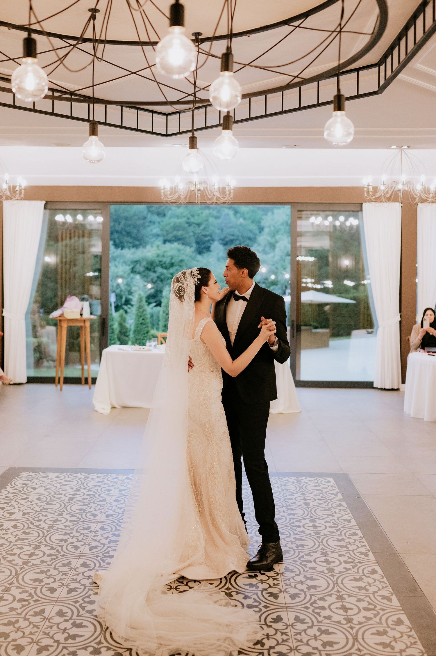 A couple dances in an elegant reception hall with modern lighting and floor design.