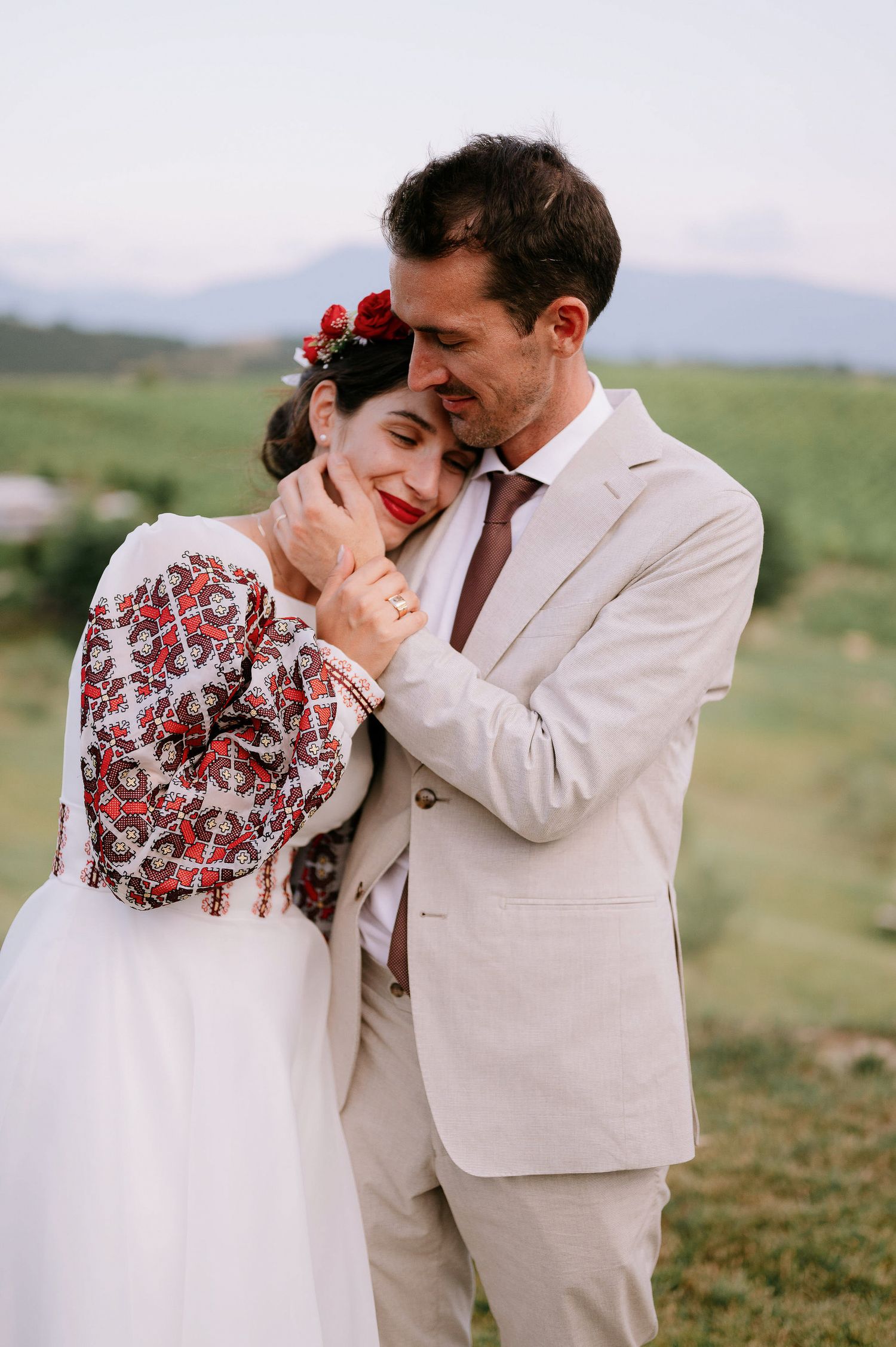 Romantic wedding photo showing tender embrace against rolling hills landscape.