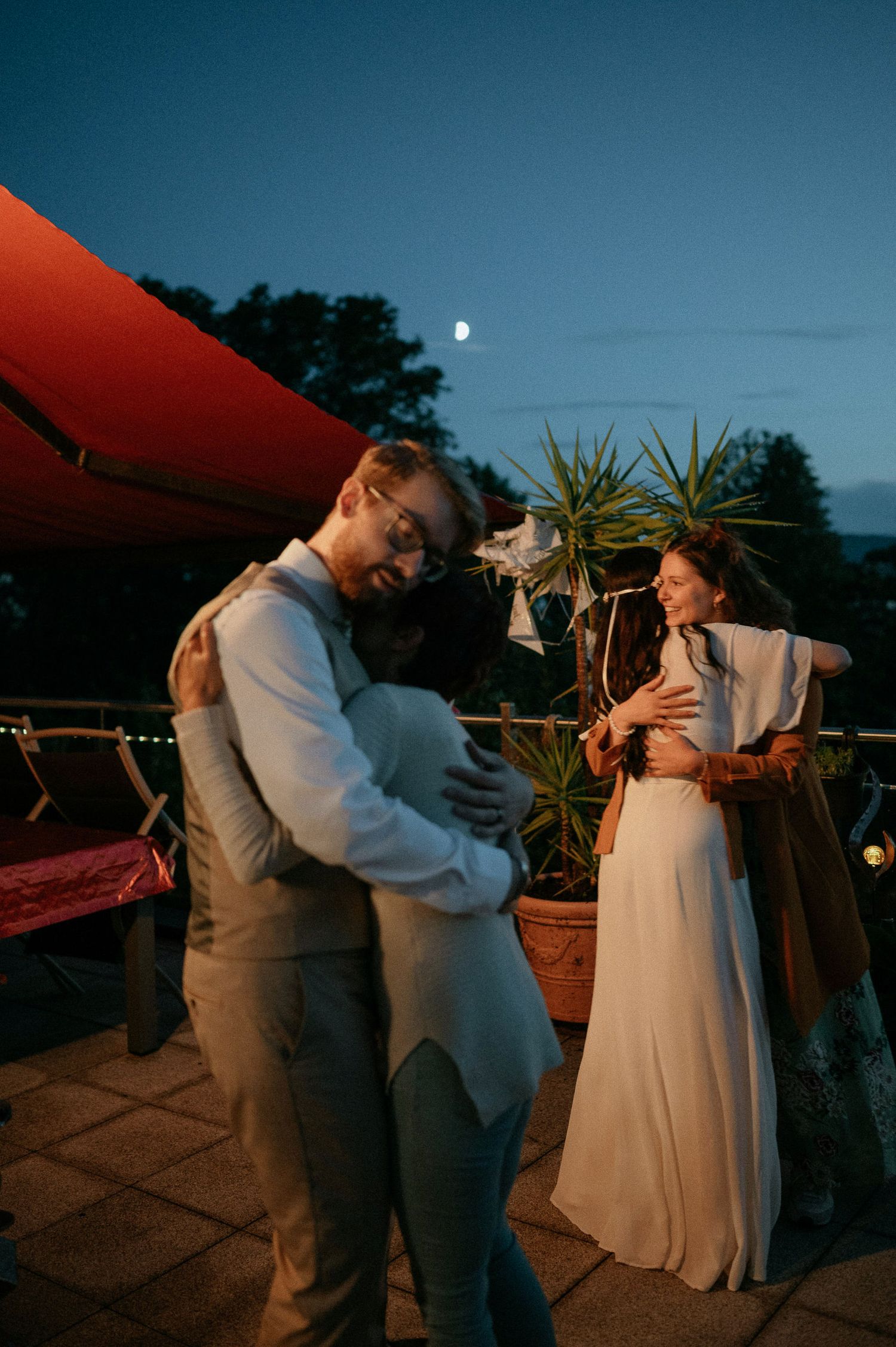 Couples dancing together on outdoor patio at dusk with string lights overhead.
