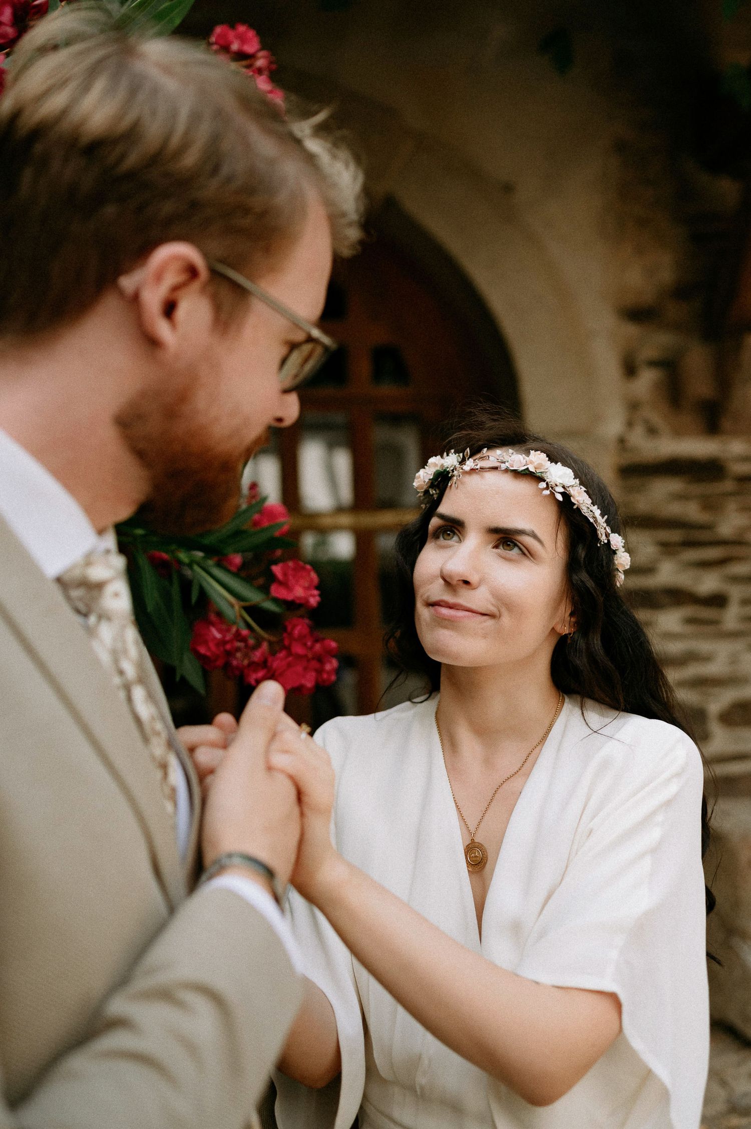 Tender wedding moment shared between a couple against a stone wall with blooming red flowers.