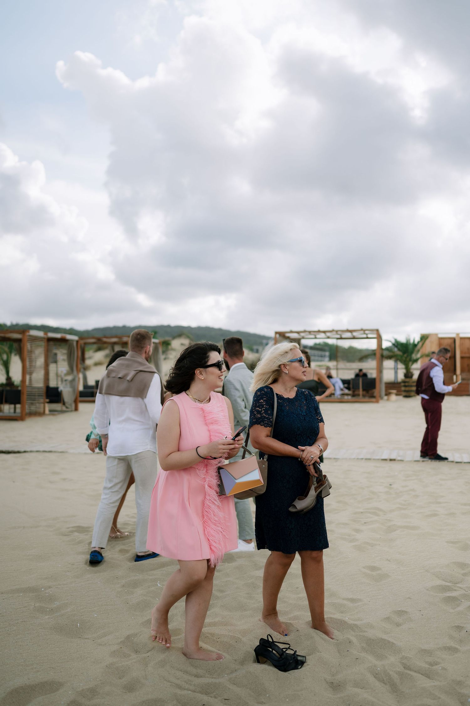 Wedding guests gather on a sandy beach under cloudy skies wearing casual attire.