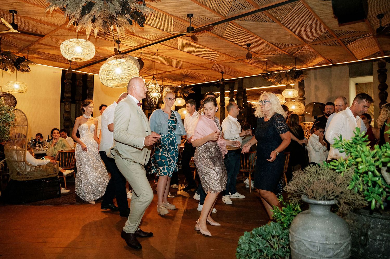 Energetic wedding guests dancing on wooden floor under warm lighting at indoor reception.