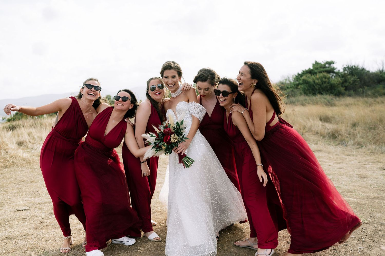 Wedding party members in burgundy dresses share candid moments outdoors.