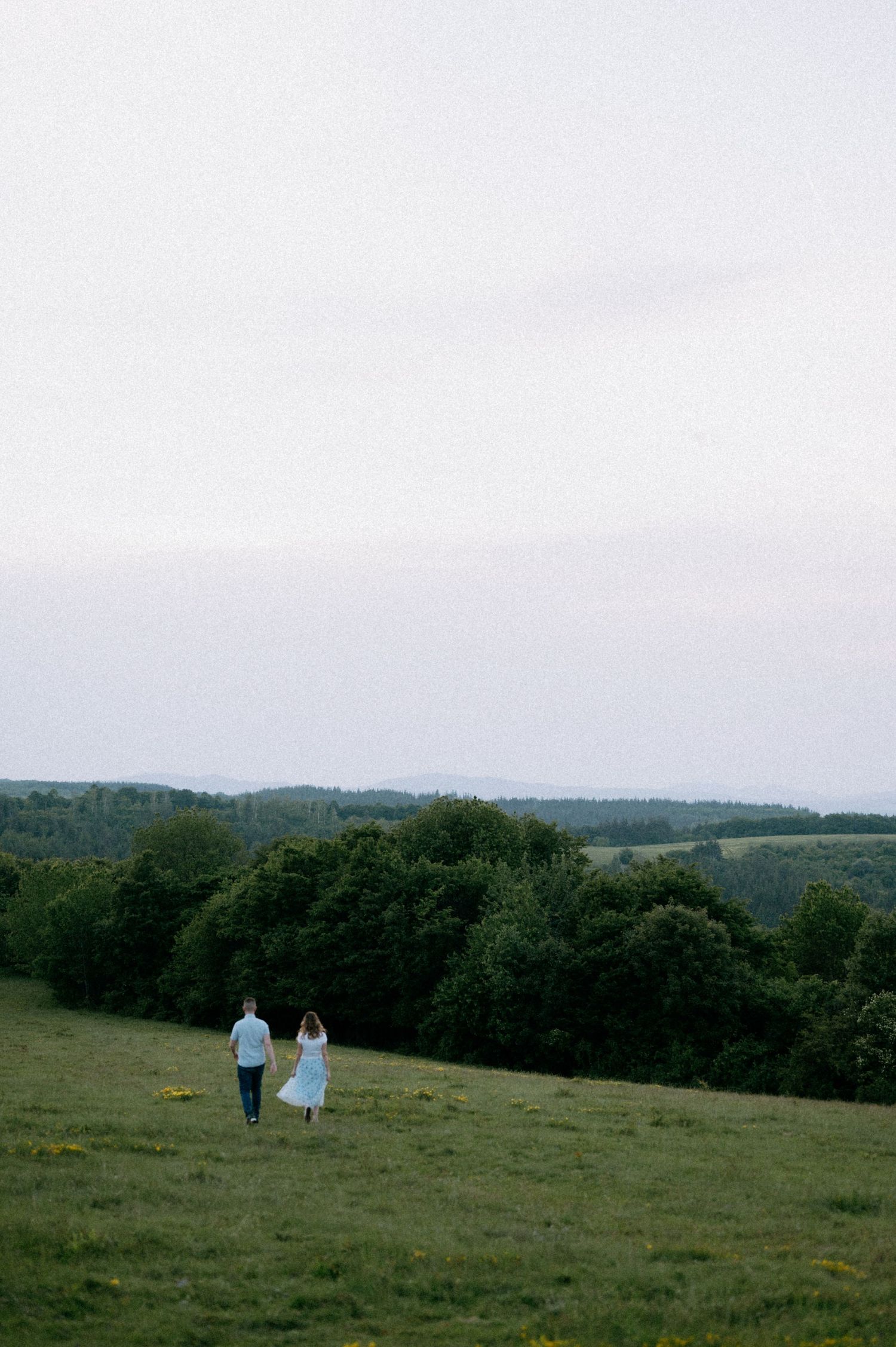 Wide landscape shot of couple walking through a remote hilltop meadow.