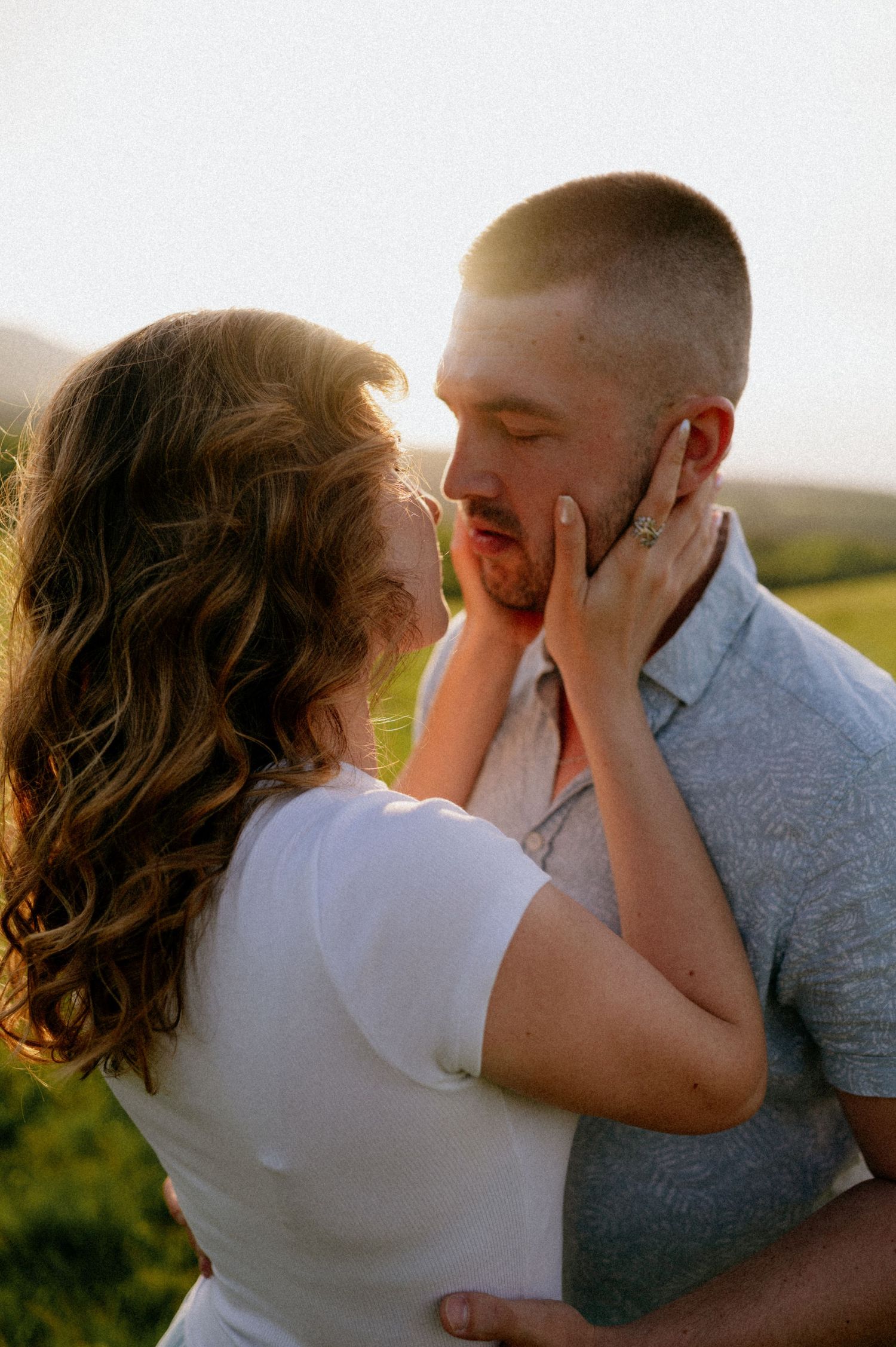 A couple holds each other's faces while sharing an intimate moment in nature.
