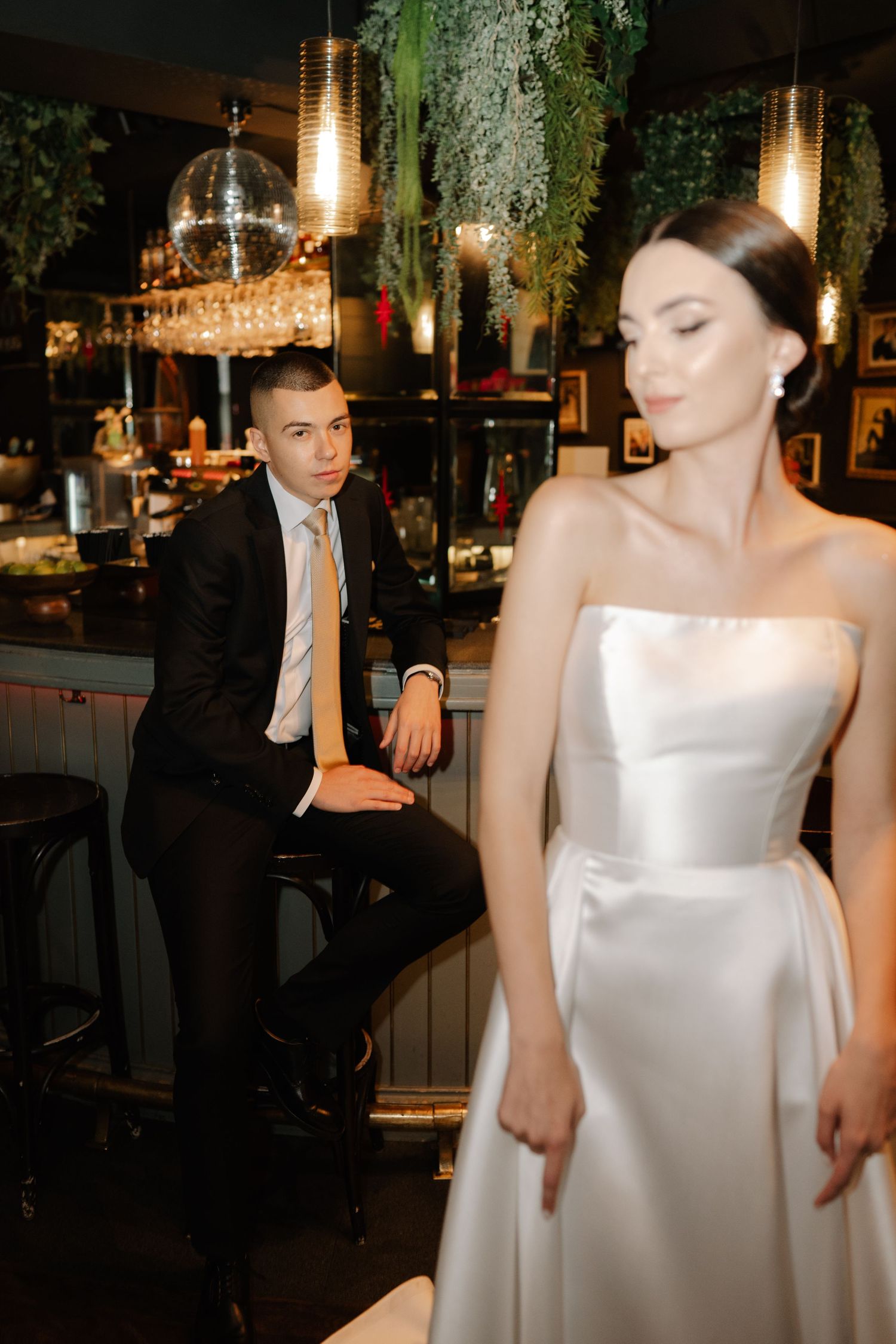 Elegant wedding scene in a restaurant with chandeliers and greenery, featuring a bride in a white strapless gown.