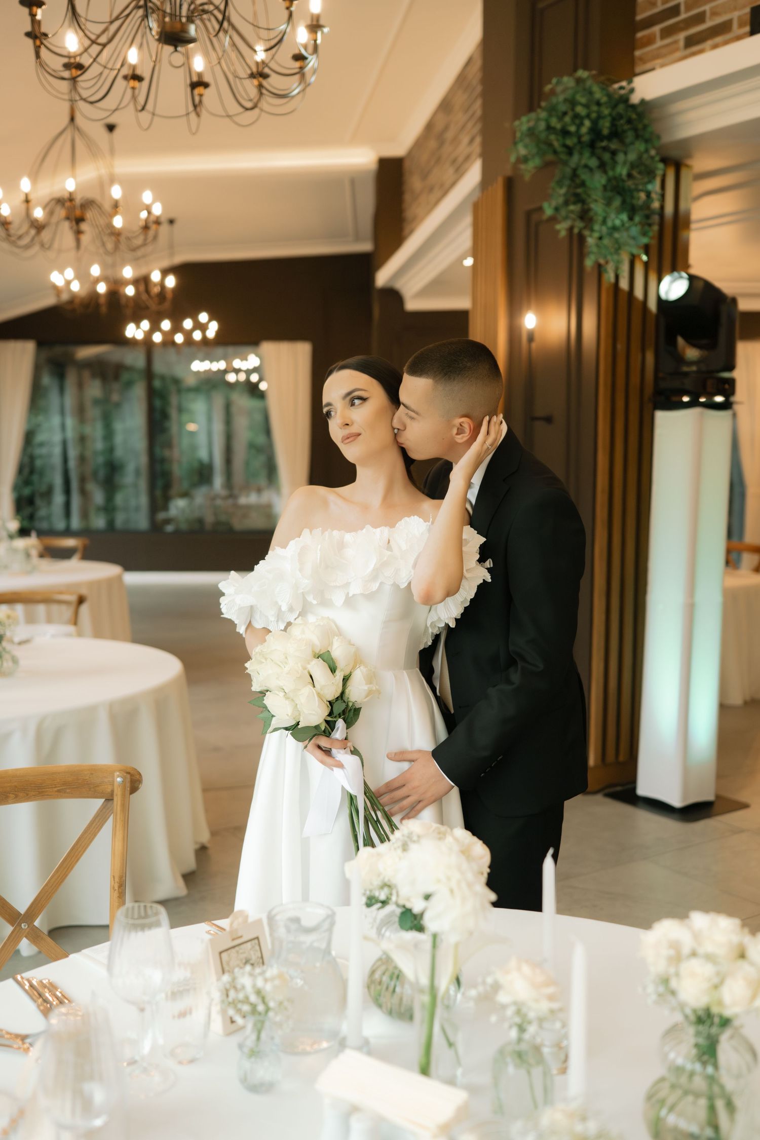 Elegant wedding reception venue with chandeliers, white floral arrangements and romantic table settings.