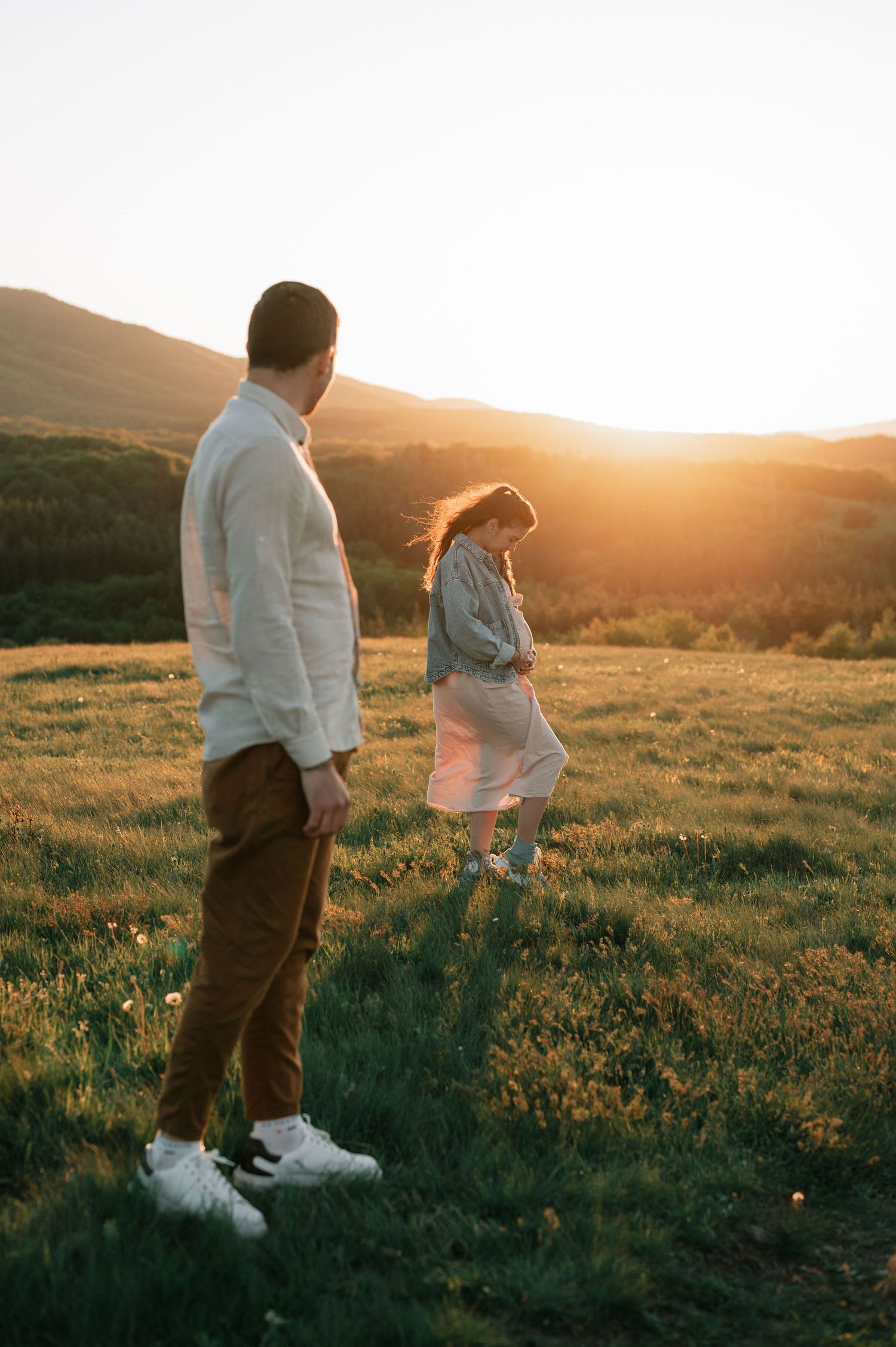 A couple stands together in a golden meadow during sunset, silhouetted against the warm evening light.