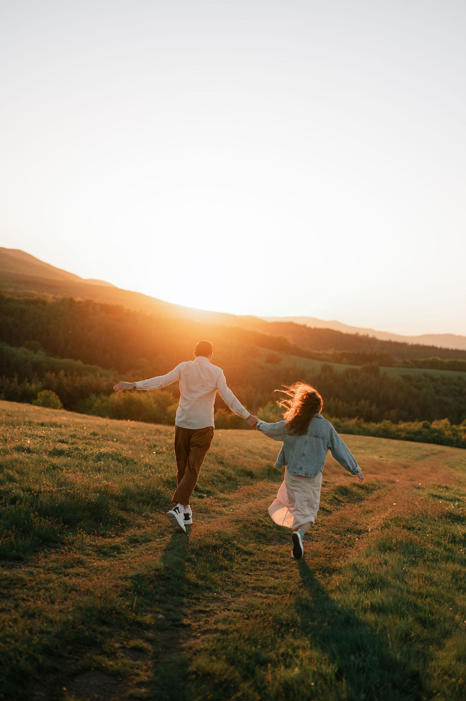 Two people dance and twirl together on a grassy hilltop at sunset, creating silhouettes against the golden sky.