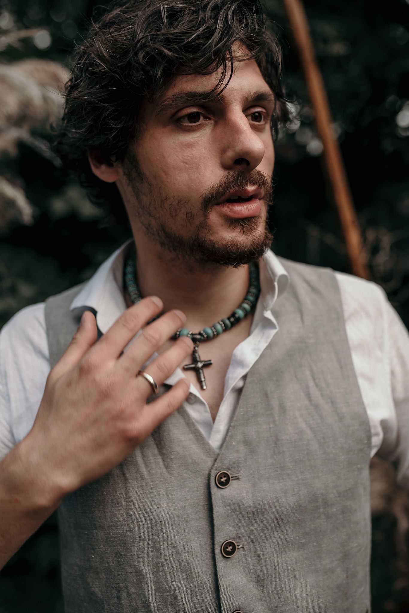Close-up shot showing details of a turquoise necklace and cross pendant against a gray vest.