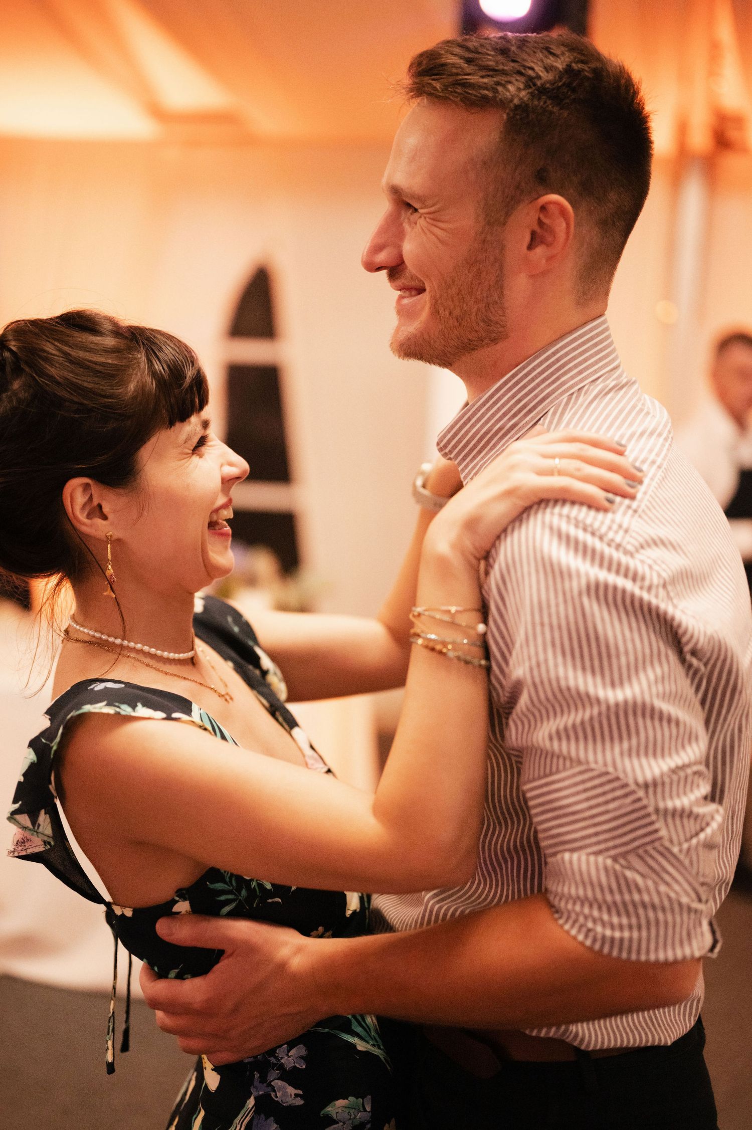 A couple dances intimately in warm lighting at a reception, showcasing romantic movement and connection.