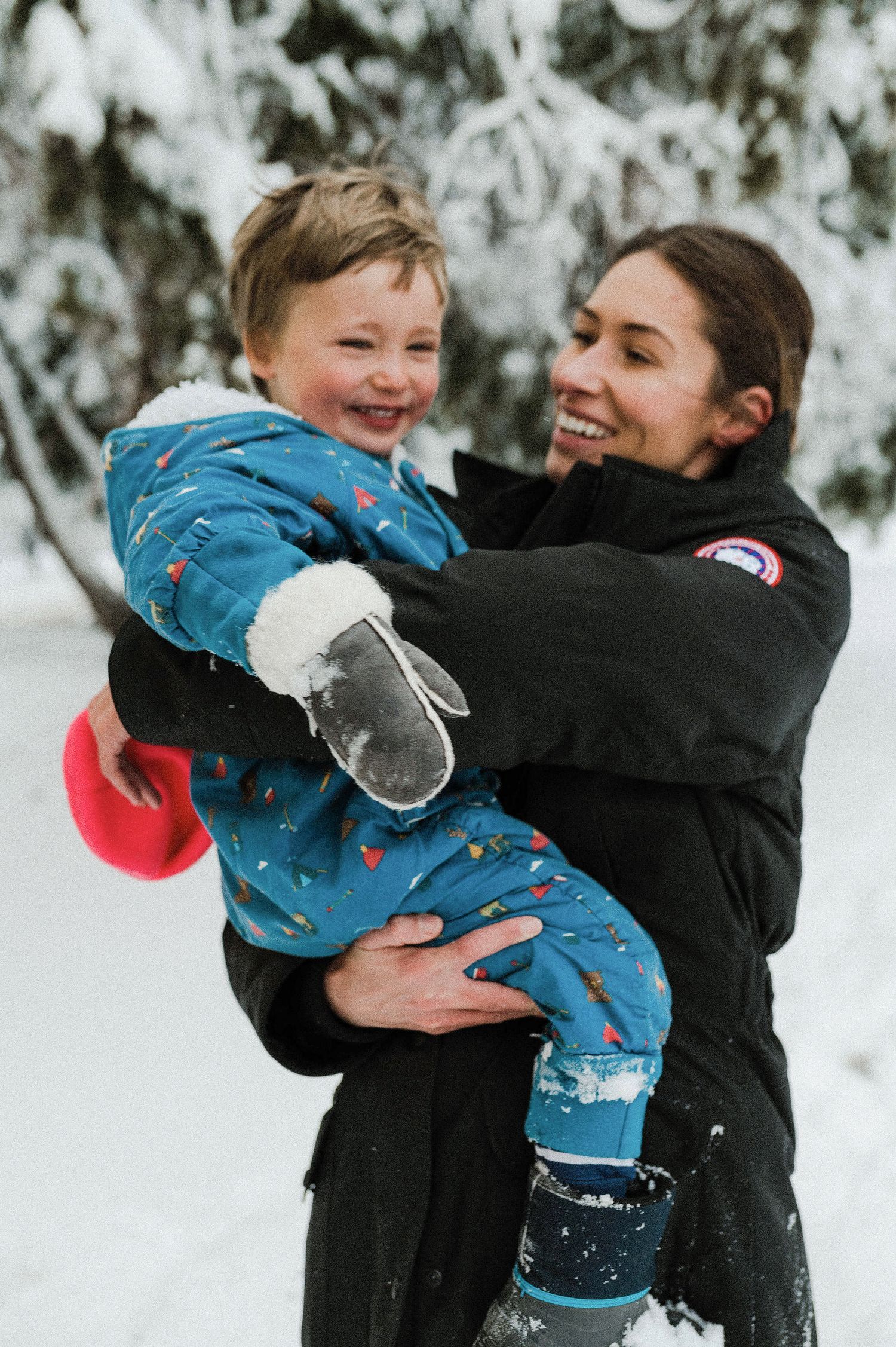 Two people share a joyful embrace in the snow while wearing winter coats and displaying genuine happiness.