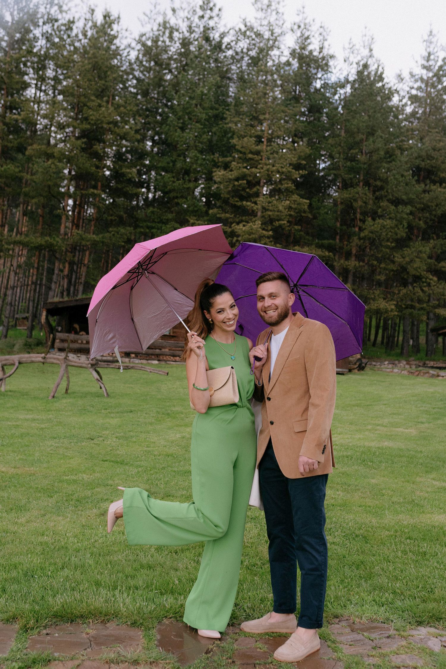 Couple shares intimate moment under purple and pink umbrellas on stone pathway.
