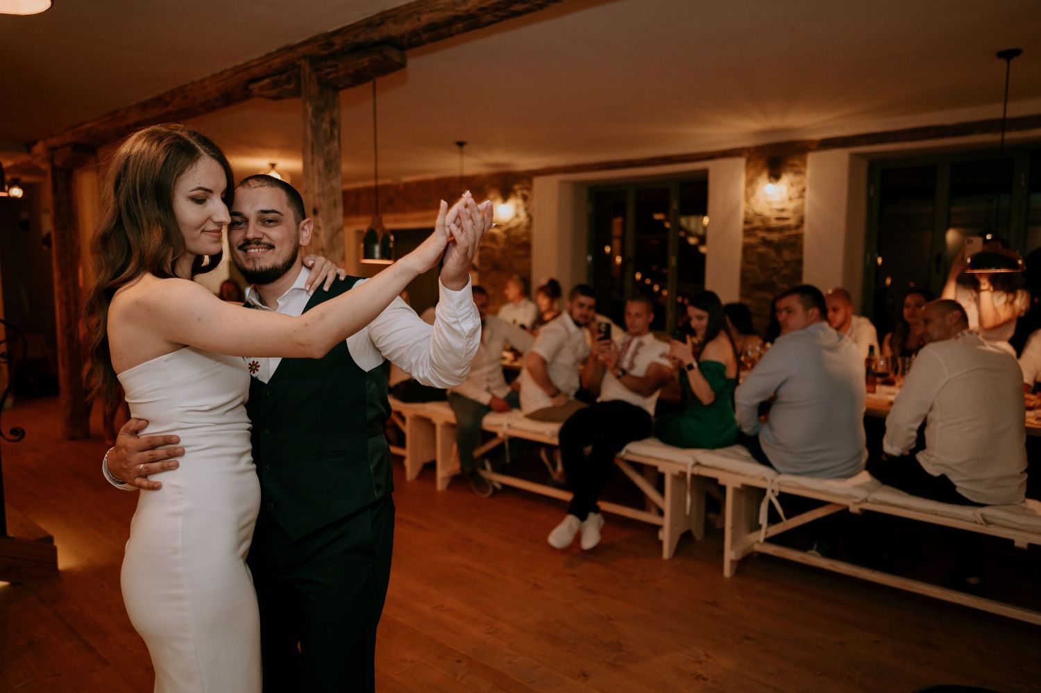 Couple performing dance steps in a warmly lit reception venue with exposed wooden beams.