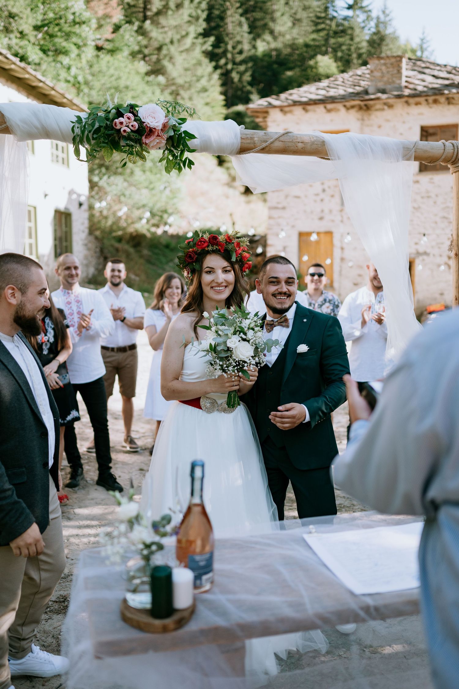 A couple celebrates during their rustic outdoor wedding ceremony while guests cheer in the background.