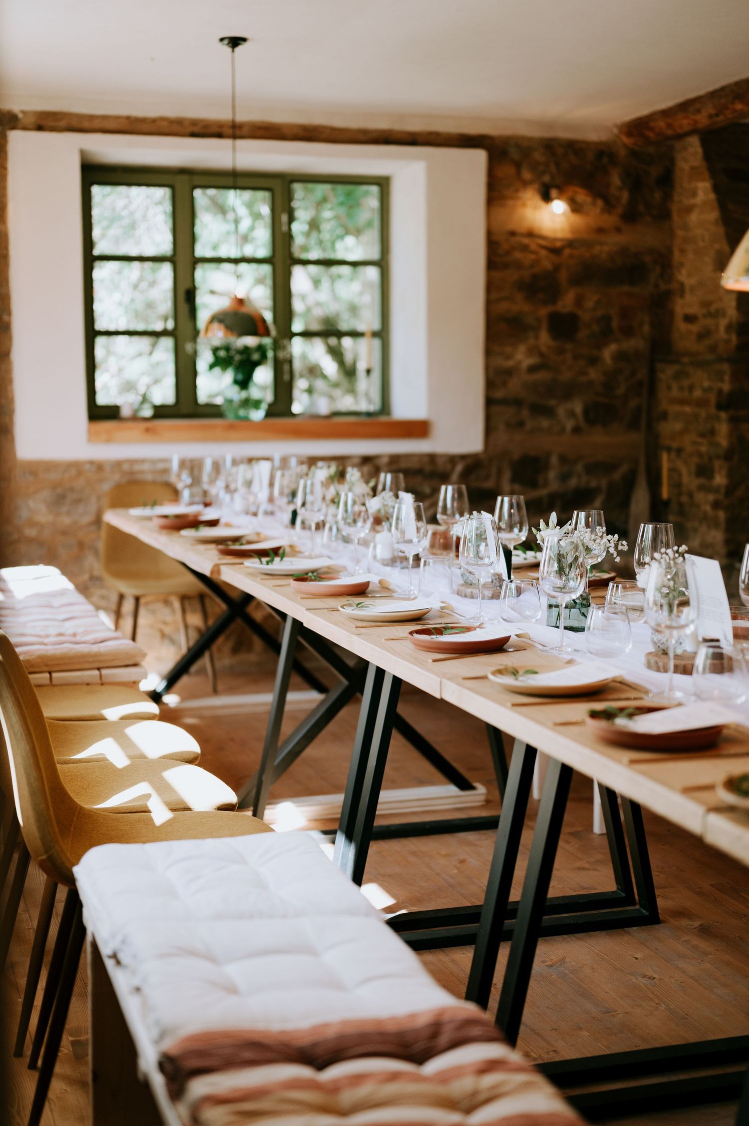 Long dining tables with crisp white linens arranged in a rustic stone-walled restaurant space.