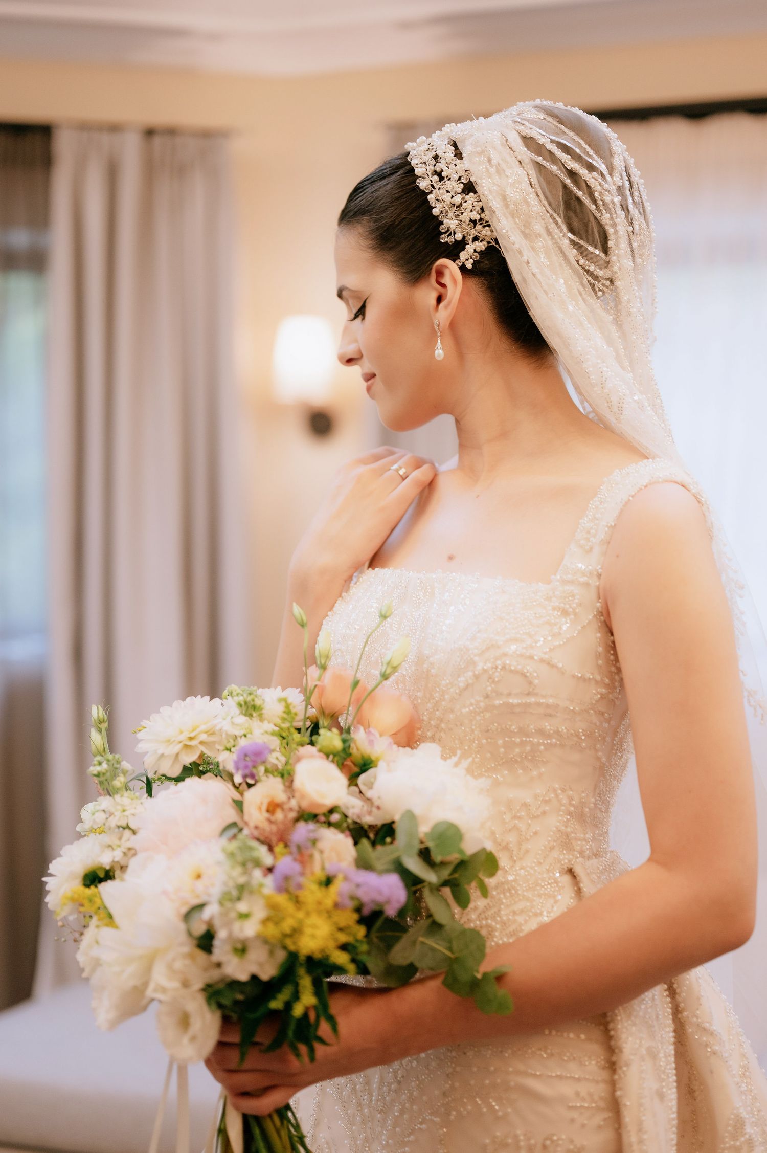 Bride in traditional white gown poses with spring bouquet featuring yellow and purple blooms.