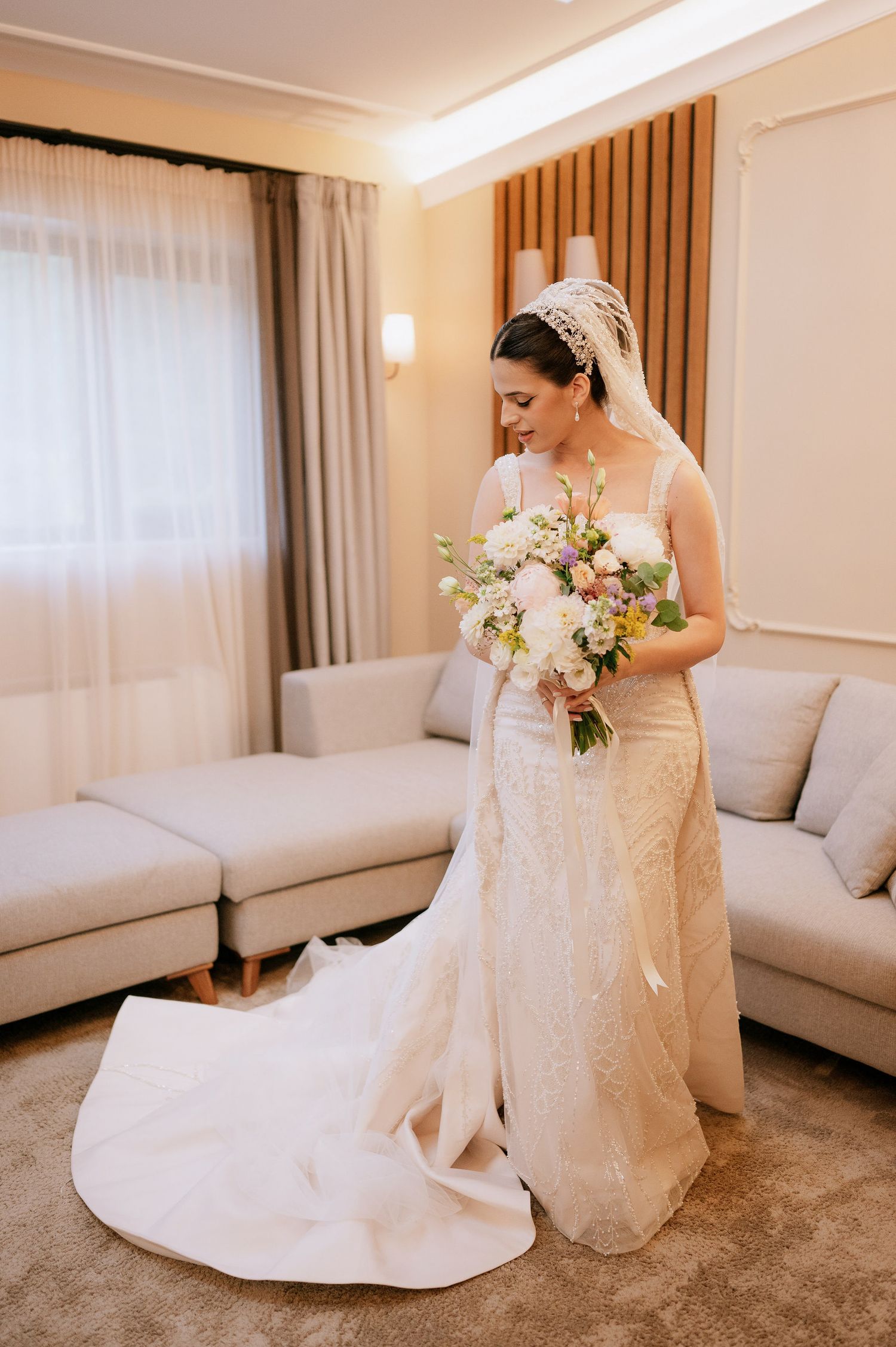 Wedding dress with dramatic train and delicate beading shown in full length as bride holds pastel bouquet.