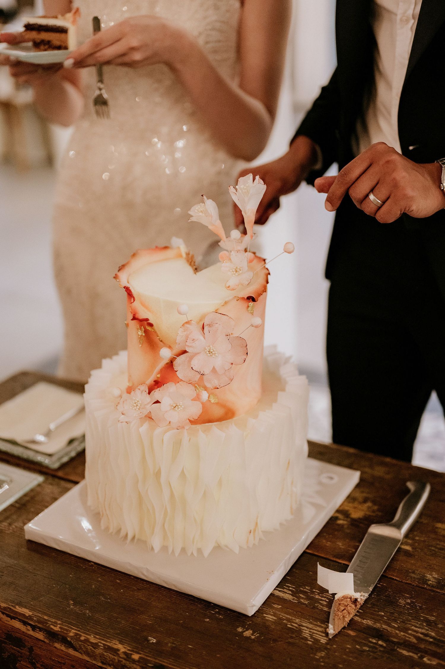 Wedding cake cutting ceremony with close-up details of the white and coral decorated cake.