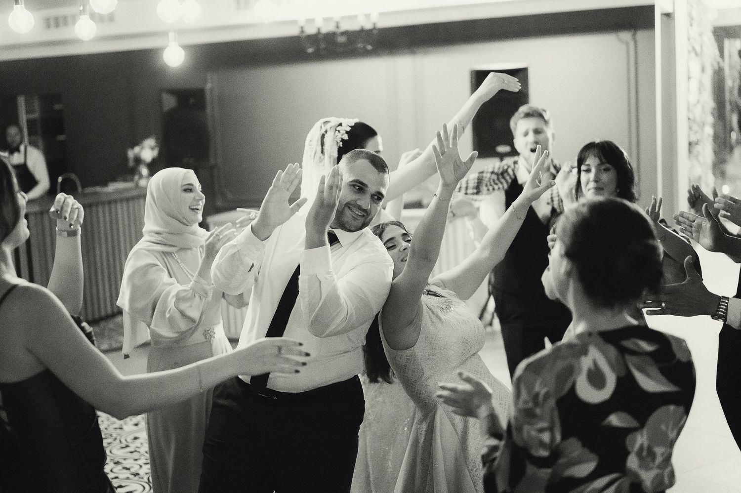 Black and white photo captures energetic dancing and celebration at an indoor event.
