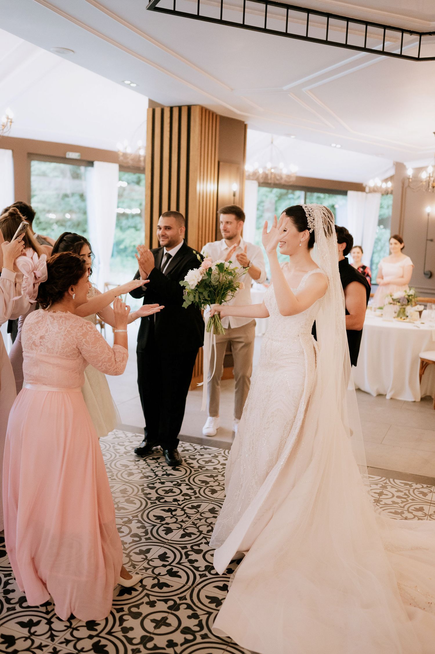 Wedding party dancing in elegant ballroom with patterned floor and wooden accents.