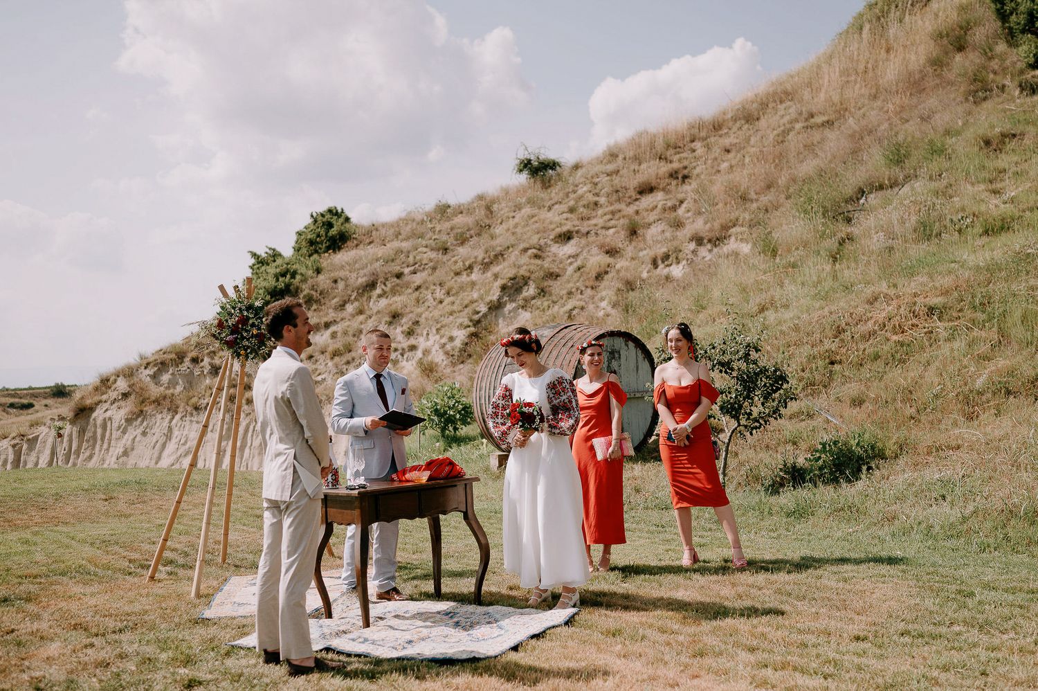 Wedding party gathered on grassy hillside with rustic ceremony setup and decorations.