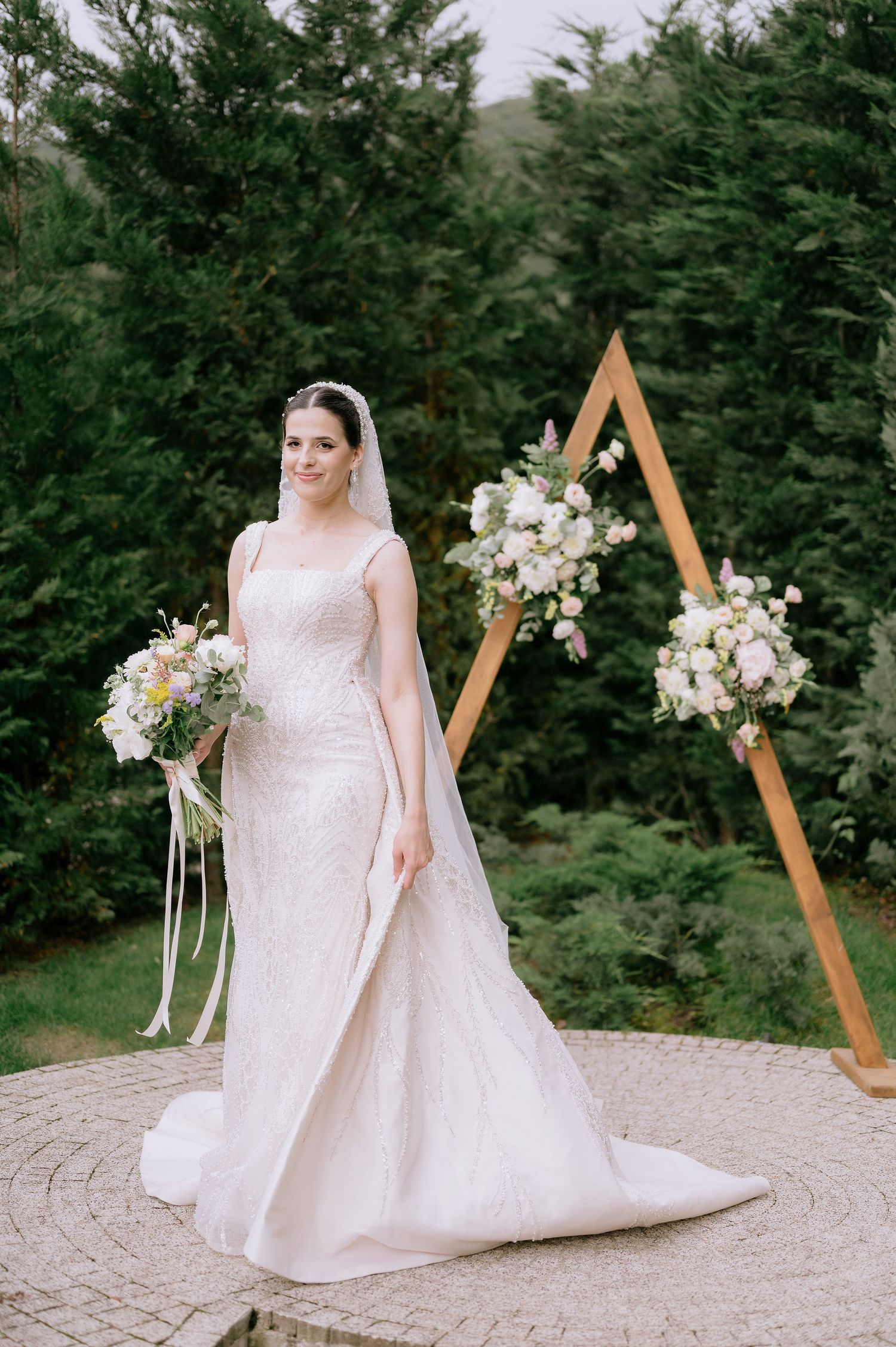 Beautiful wedding dress with long train photographed on stone patio with wooden ceremony arch.