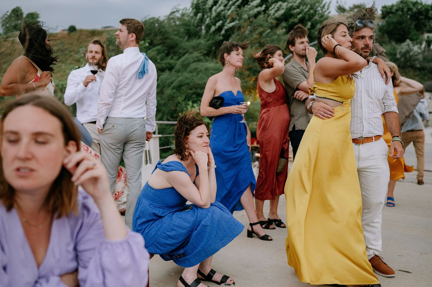 Wedding guests in colorful attire react during an outdoor celebration.