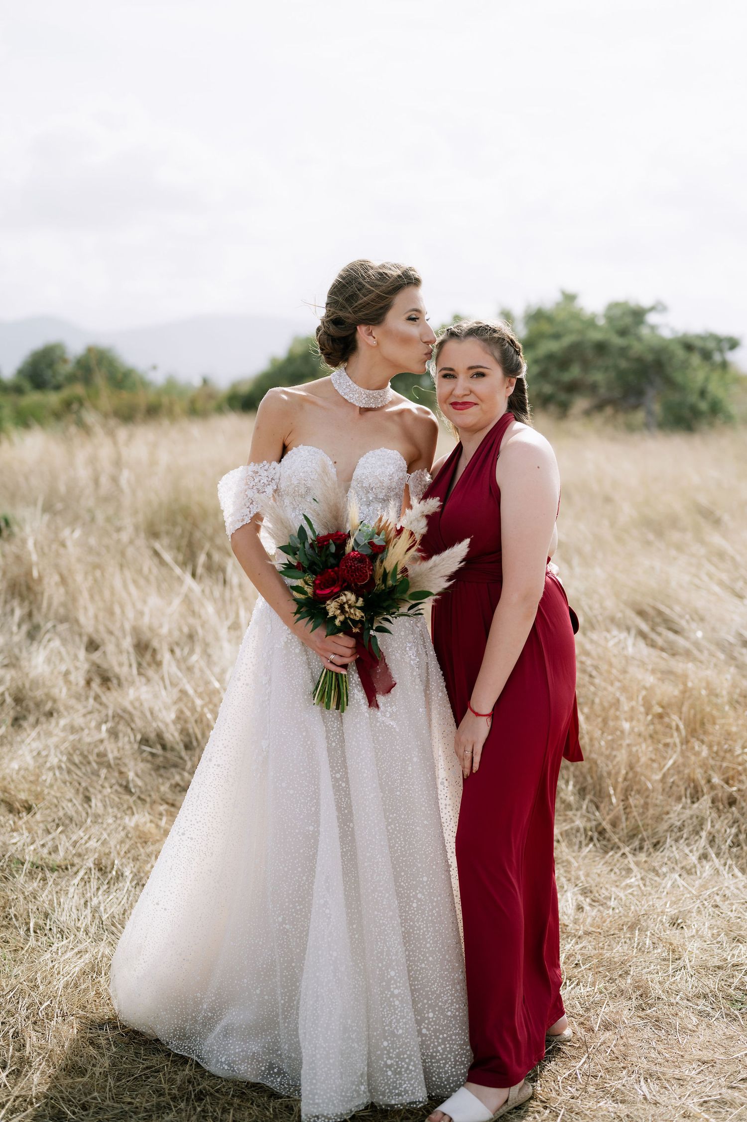 Wedding party in white and burgundy dresses holding bouquets in a field.