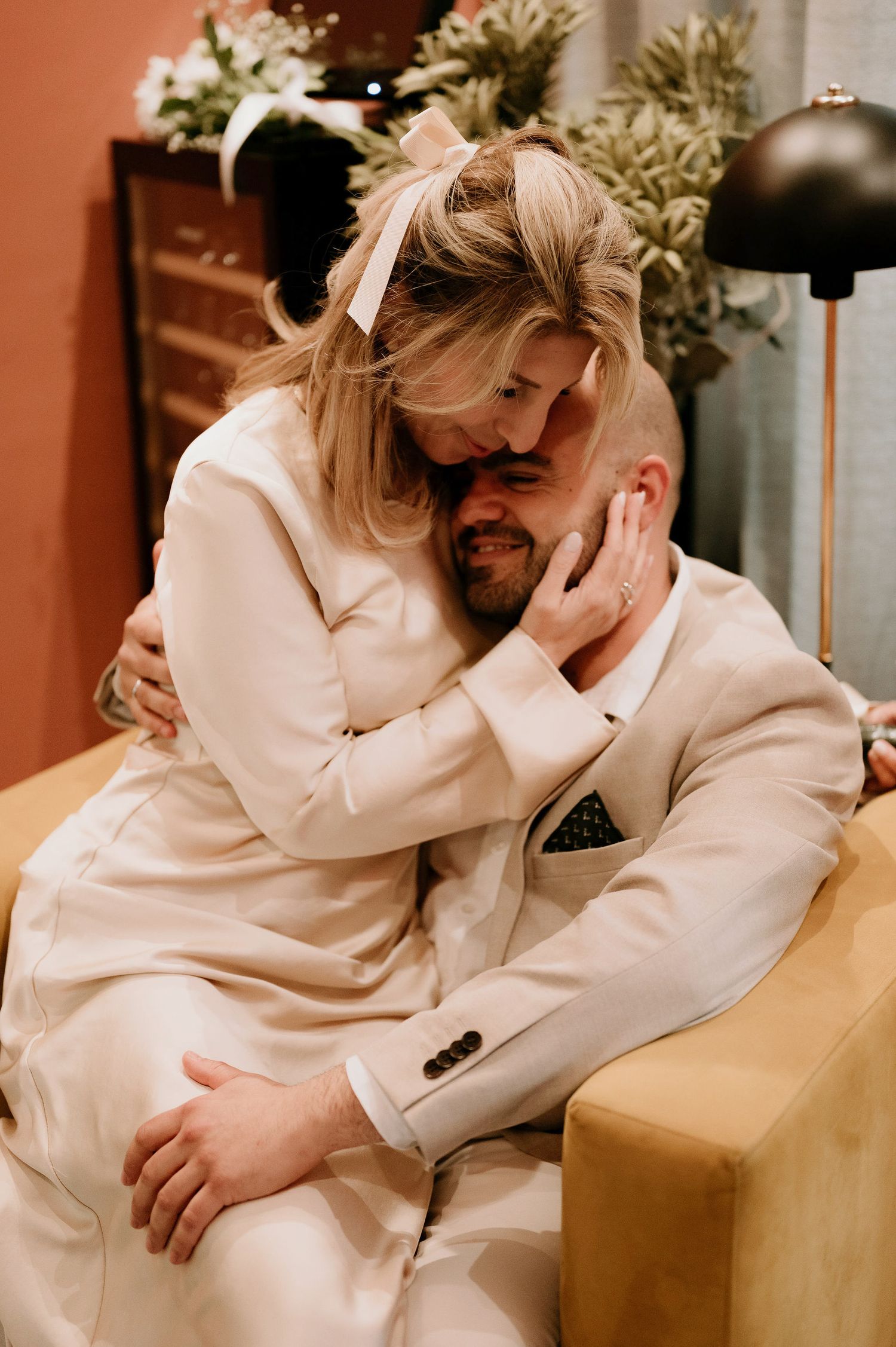 A romantic couple in white attire sharing an intimate moment on a couch.