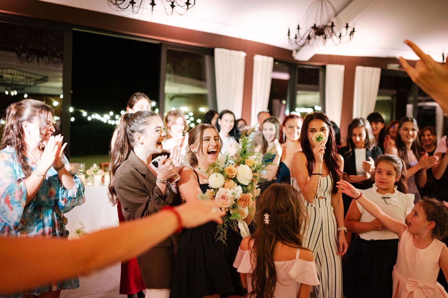 Party guests react enthusiastically during a celebration in an indoor venue with warm lighting.