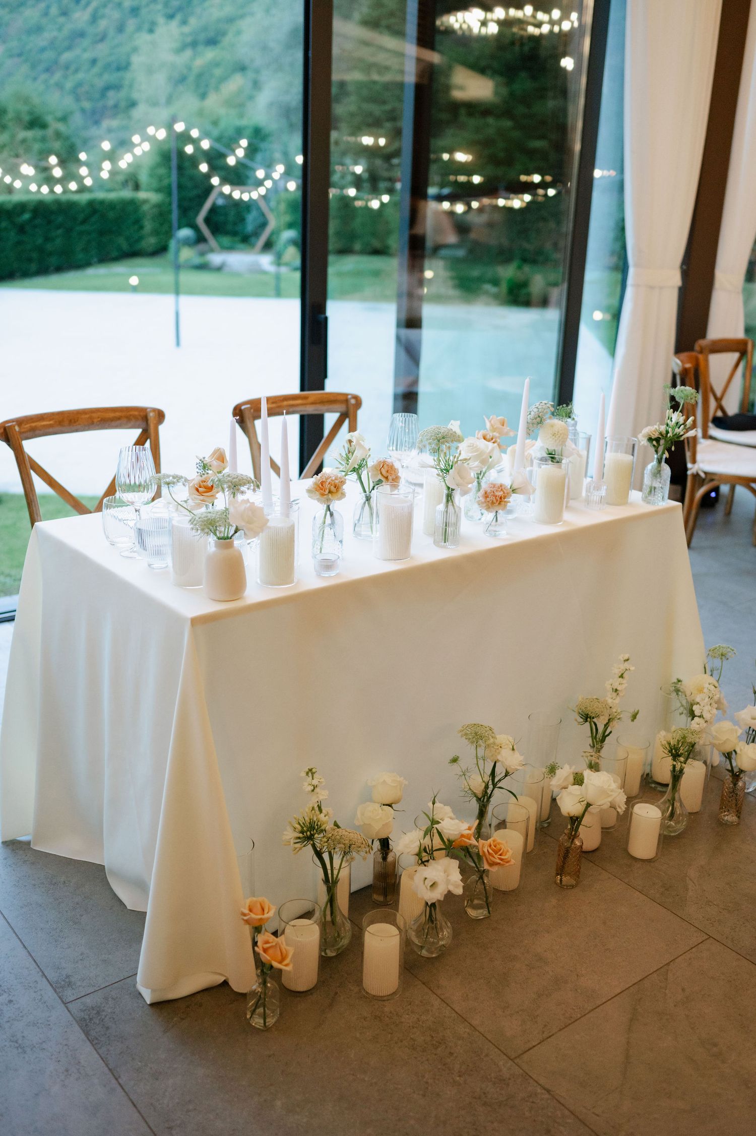 Wedding reception setup with white tablecloths and delicate floral centerpieces against panoramic mountain views.