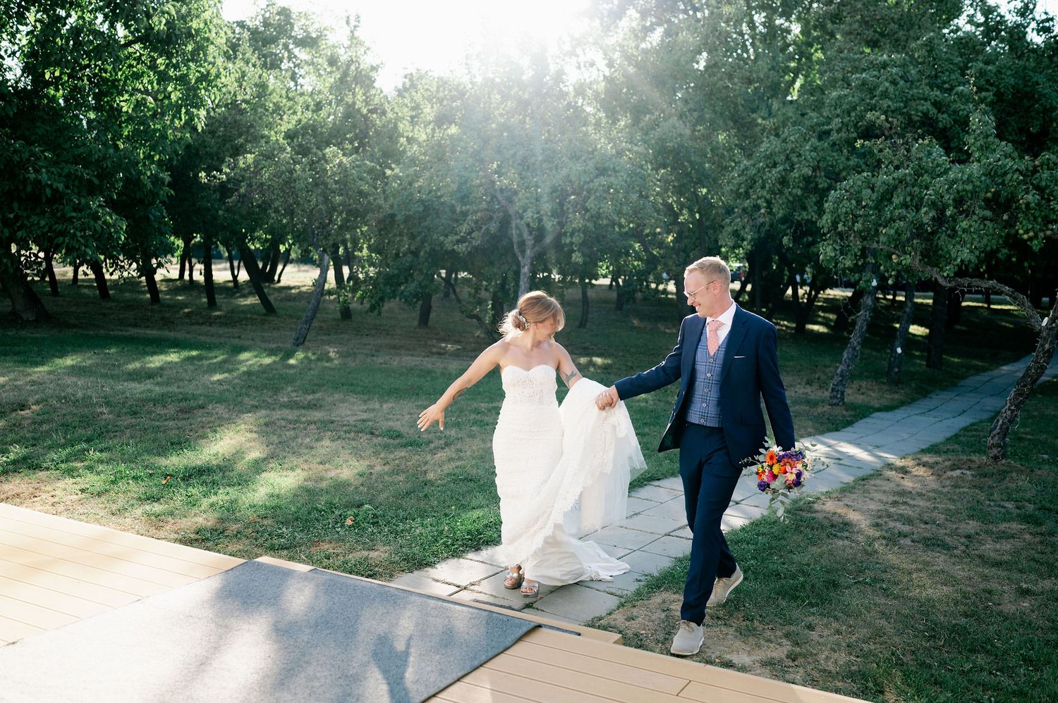 Couple joyfully walks hand in hand down a sunlit pathway during their wedding.
