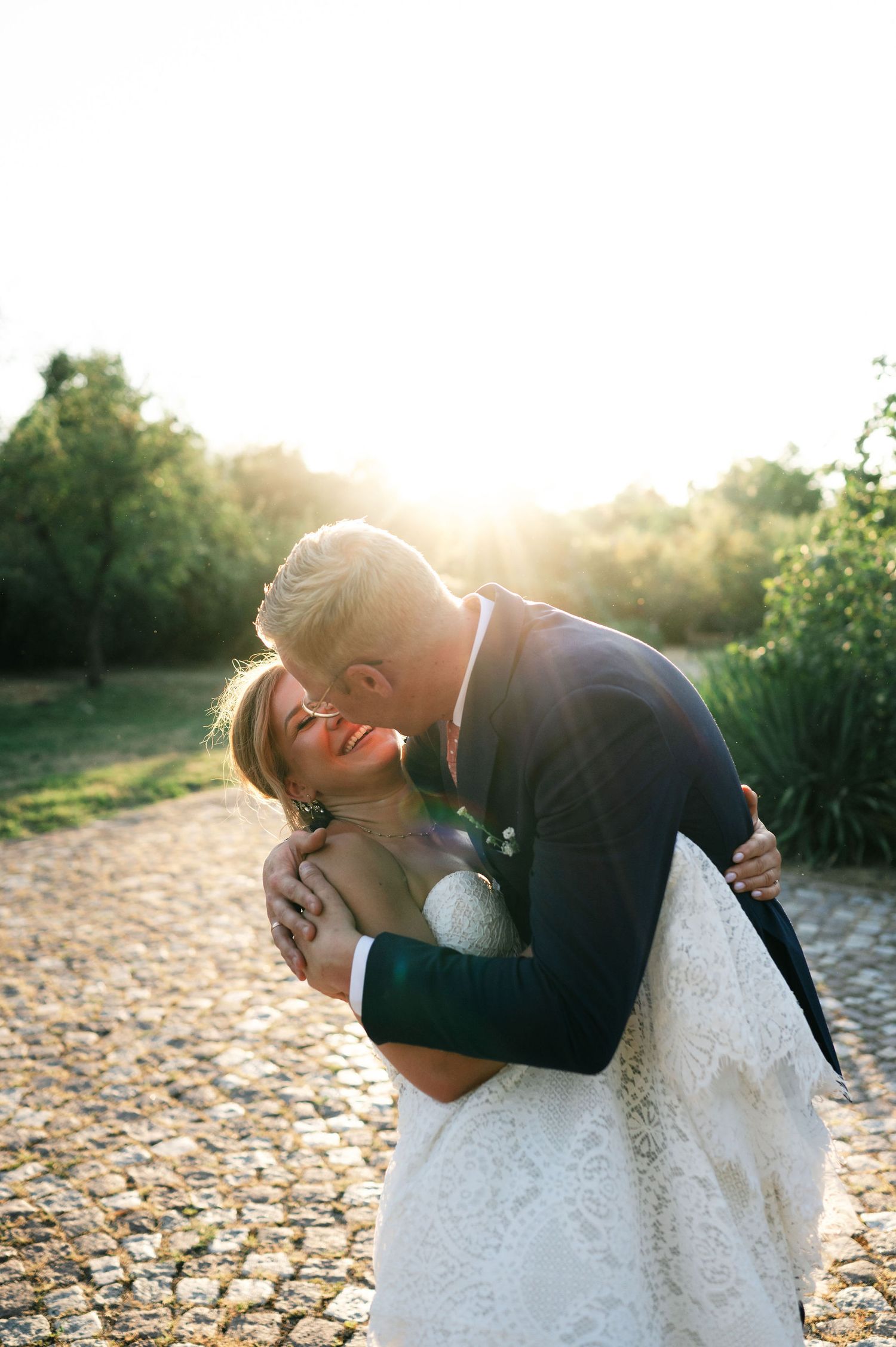 Wedding couple embraces romantically against golden sunlight on stone pathway.