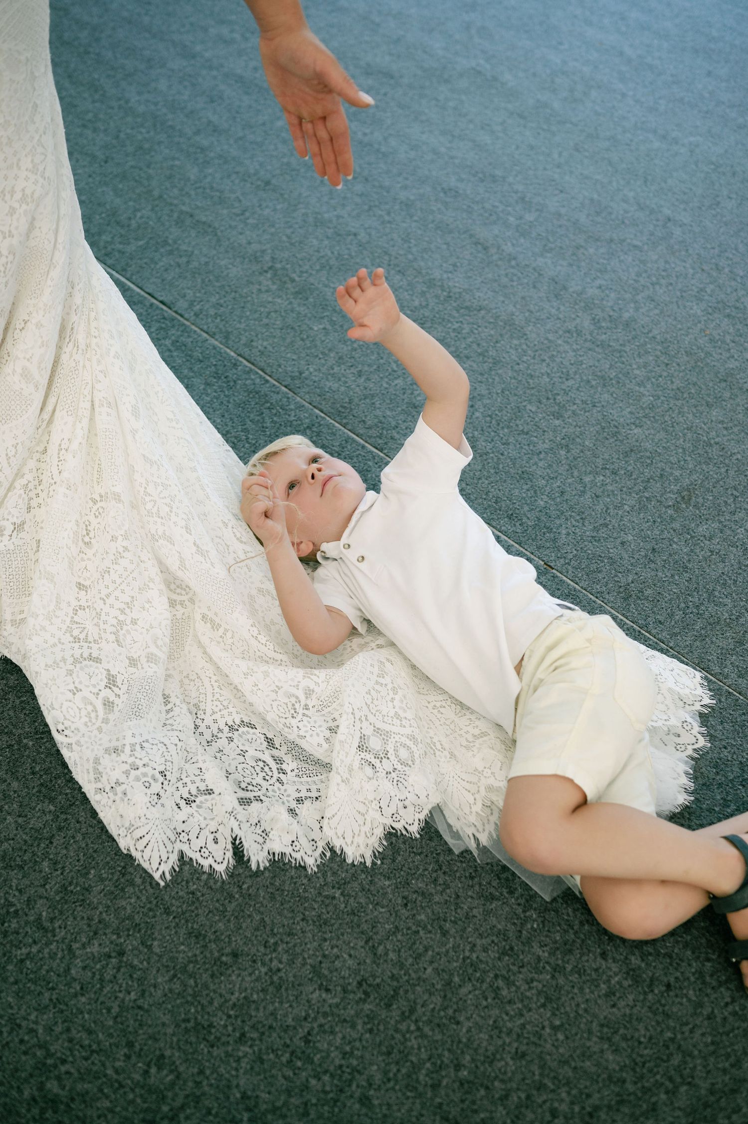 A person lying on gray carpet next to flowing white lace fabric.